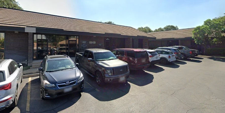 Parking lot with several cars parked in front of a single-story brick office building.