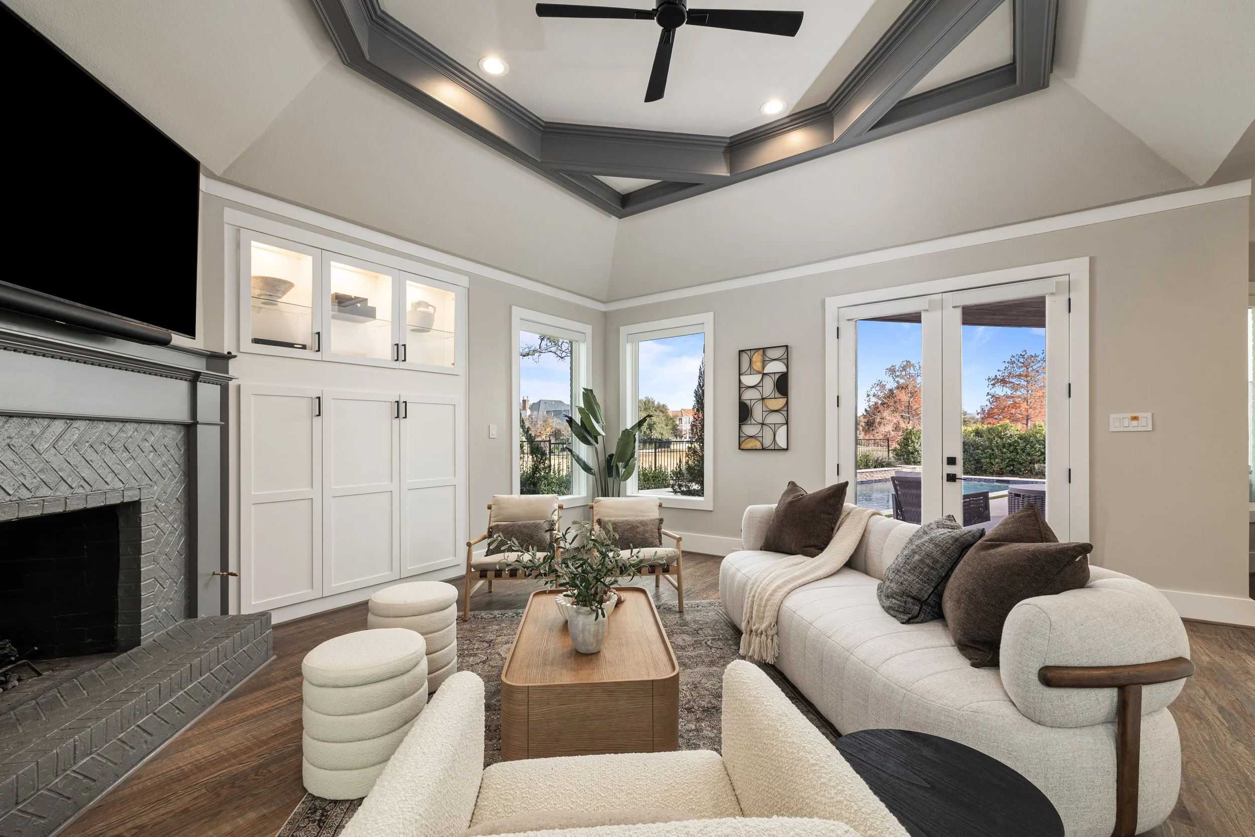 Living room with beige sofa, armchair, coffee table, fireplace, built-in cabinets, and large windows with patio view.