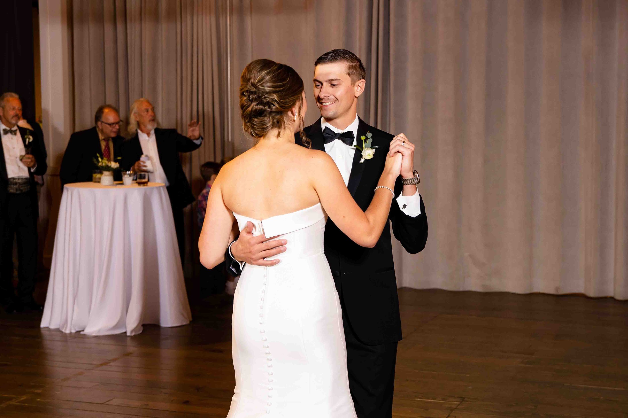 A bride and groom dance together at their wedding reception, with guests in the background enjoying the event.