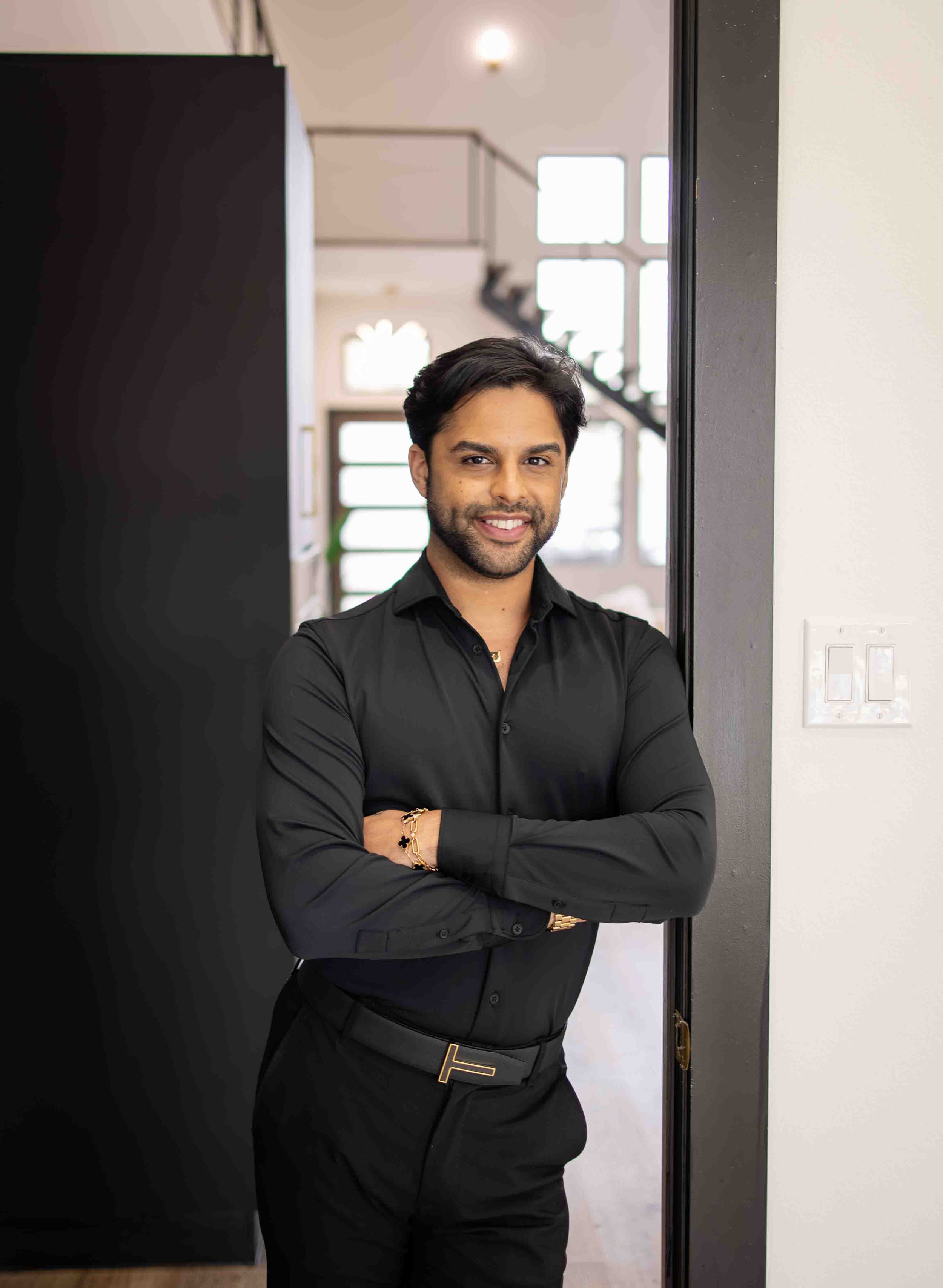 Man in black clothing standing with folded arms in a modern interior