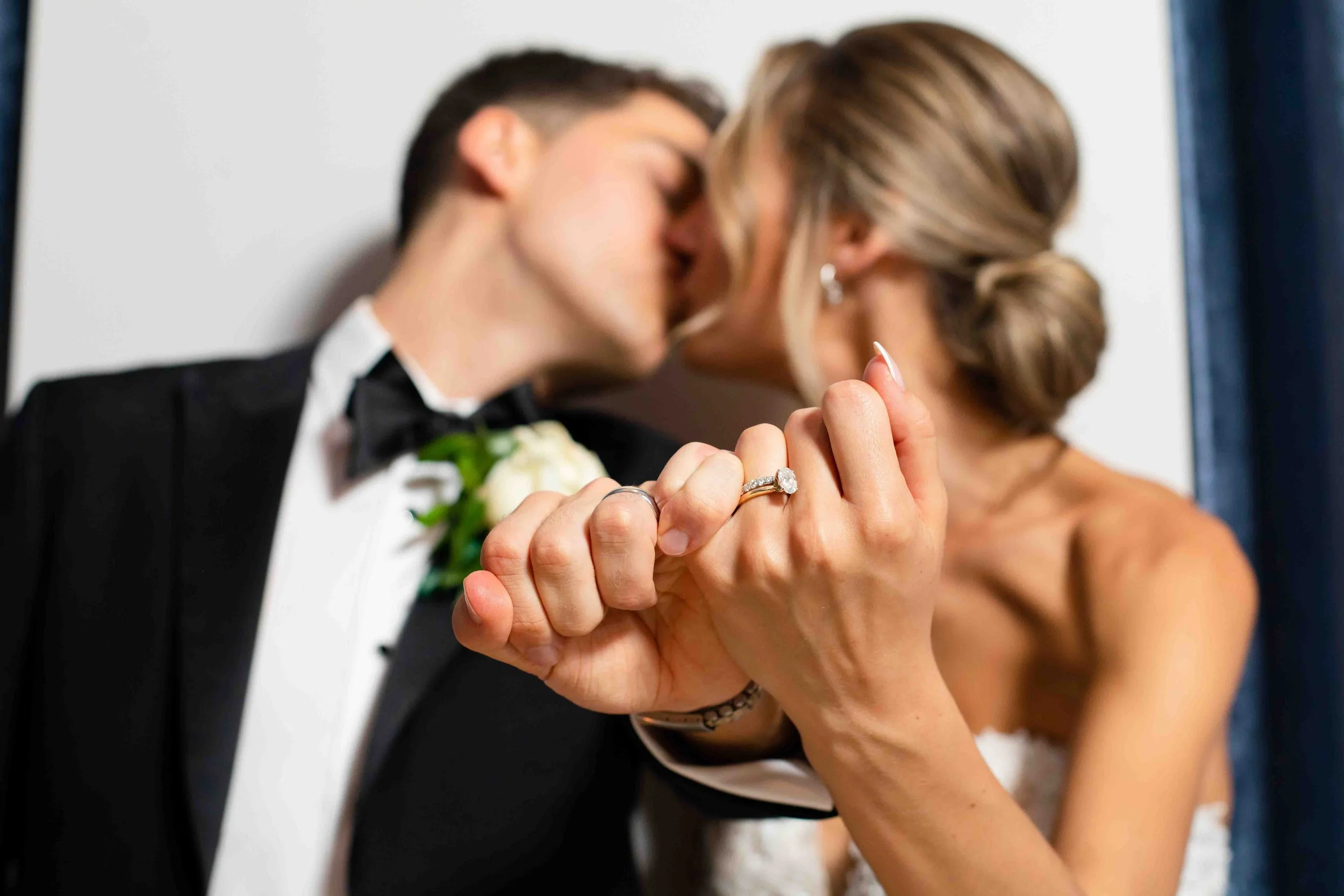 A newlywed couple is kissing, with the bride showing her engagement and wedding rings prominently on her hand.