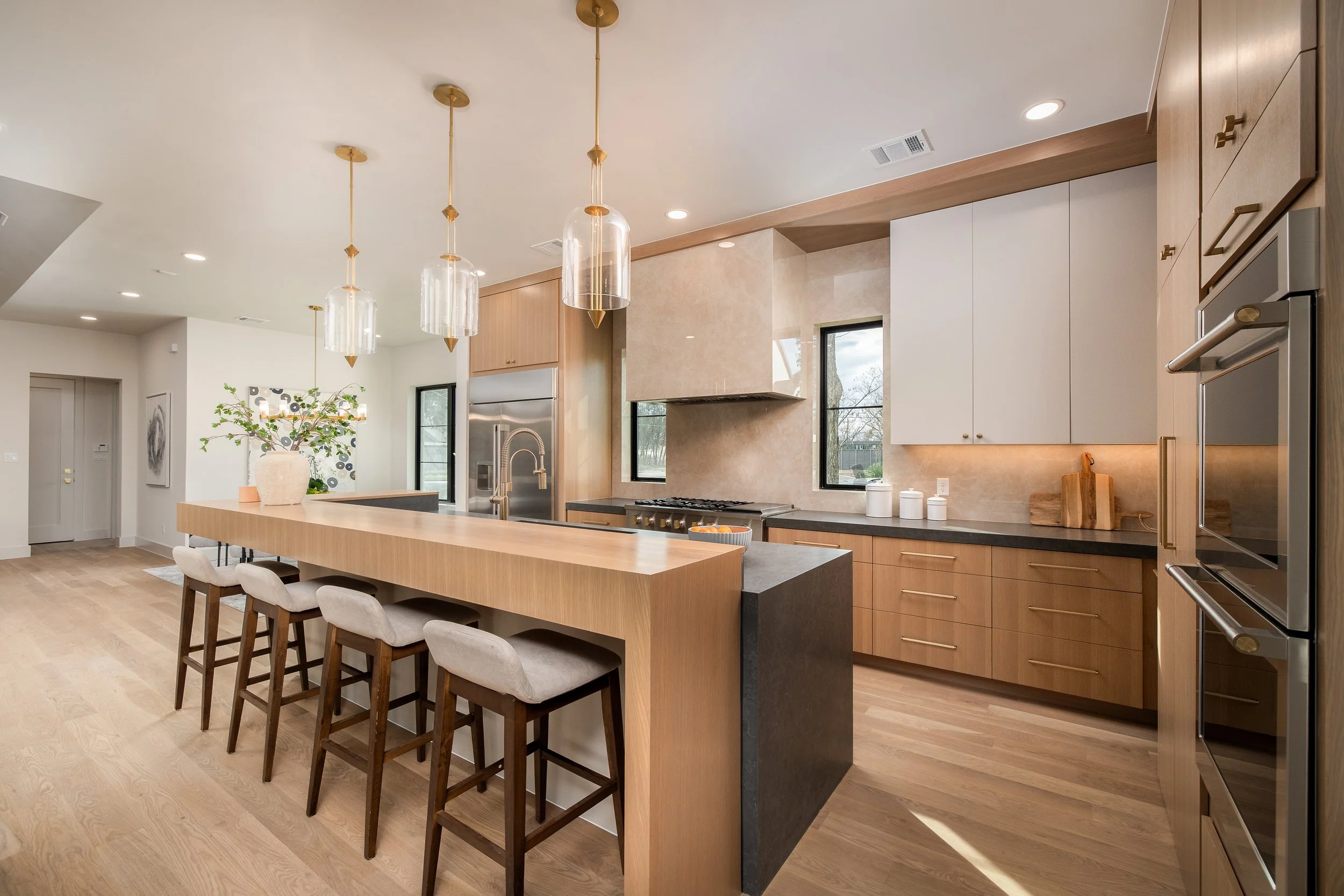 Modern kitchen with wooden cabinets, black countertops, a large island with ample seating, pendant lights, and stainless steel appliances.