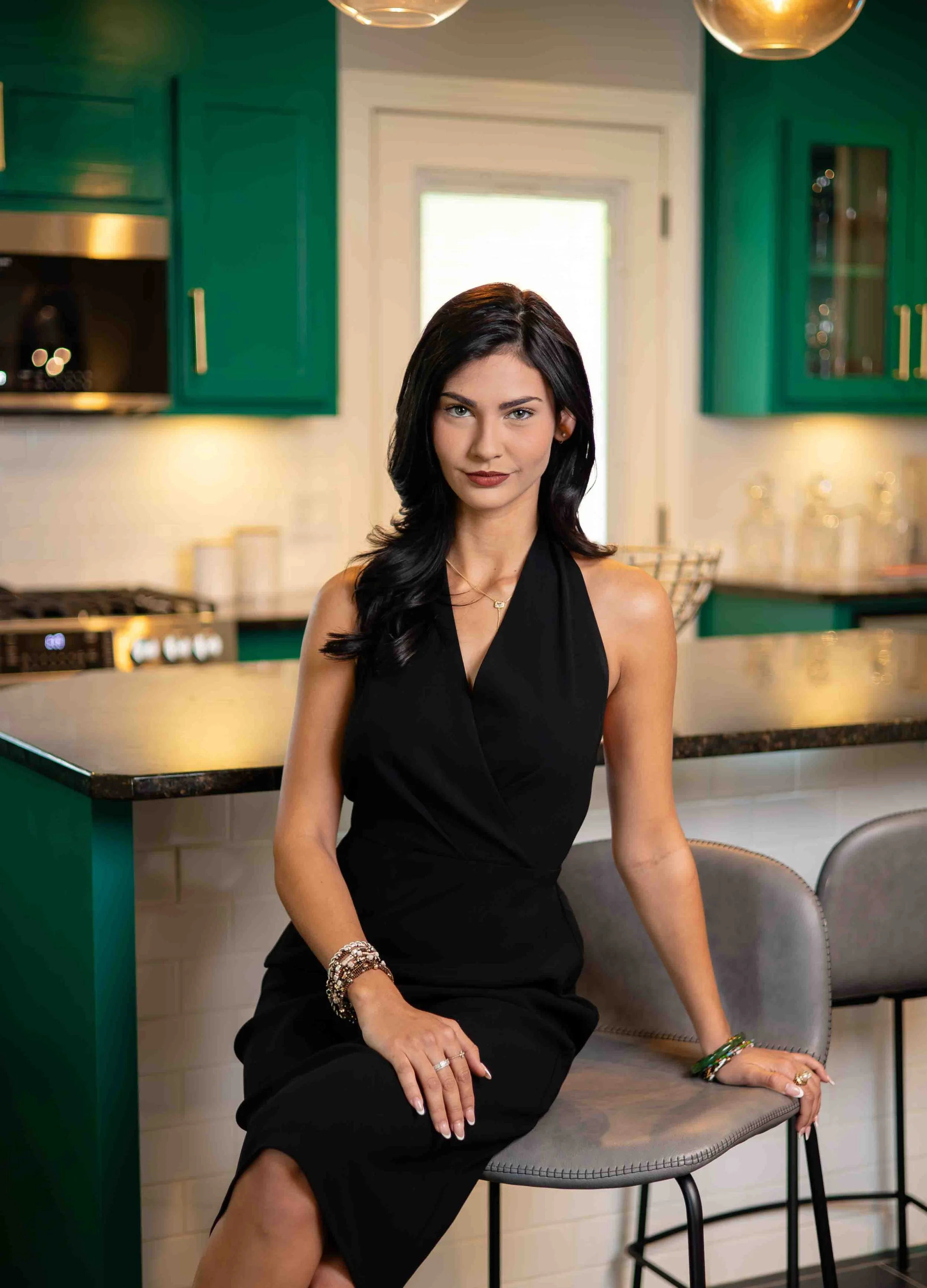 Woman in a black dress sitting in a modern kitchen with green cabinets.