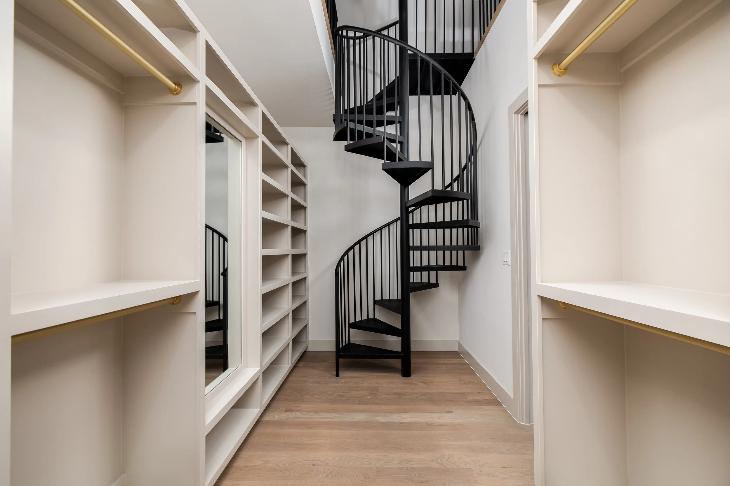 Walk-in closet with white shelving, a mirror, and a black spiral staircase.