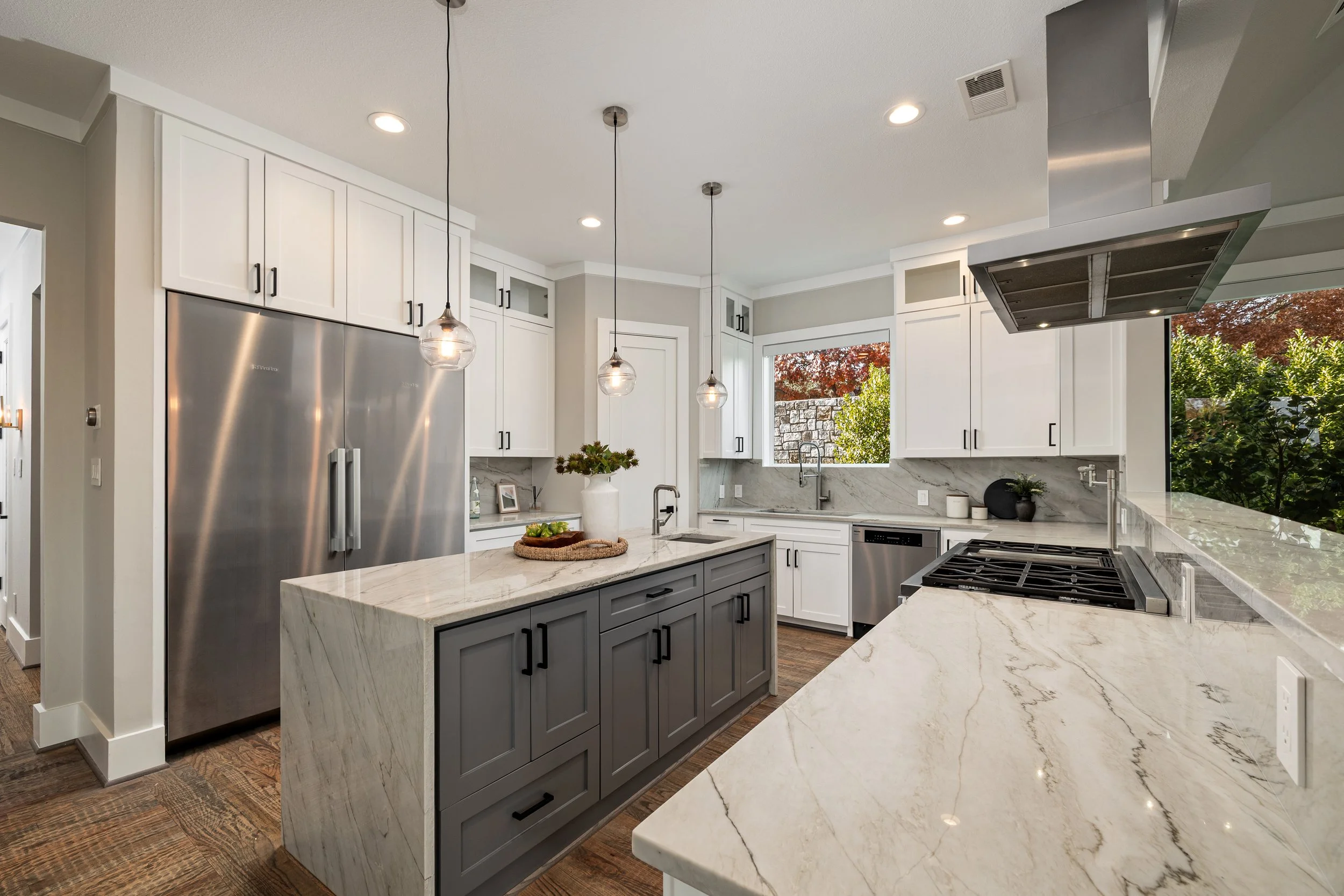 Modern kitchen with white cabinets, gray island, marble countertops, stainless steel appliances, and pendant lights.