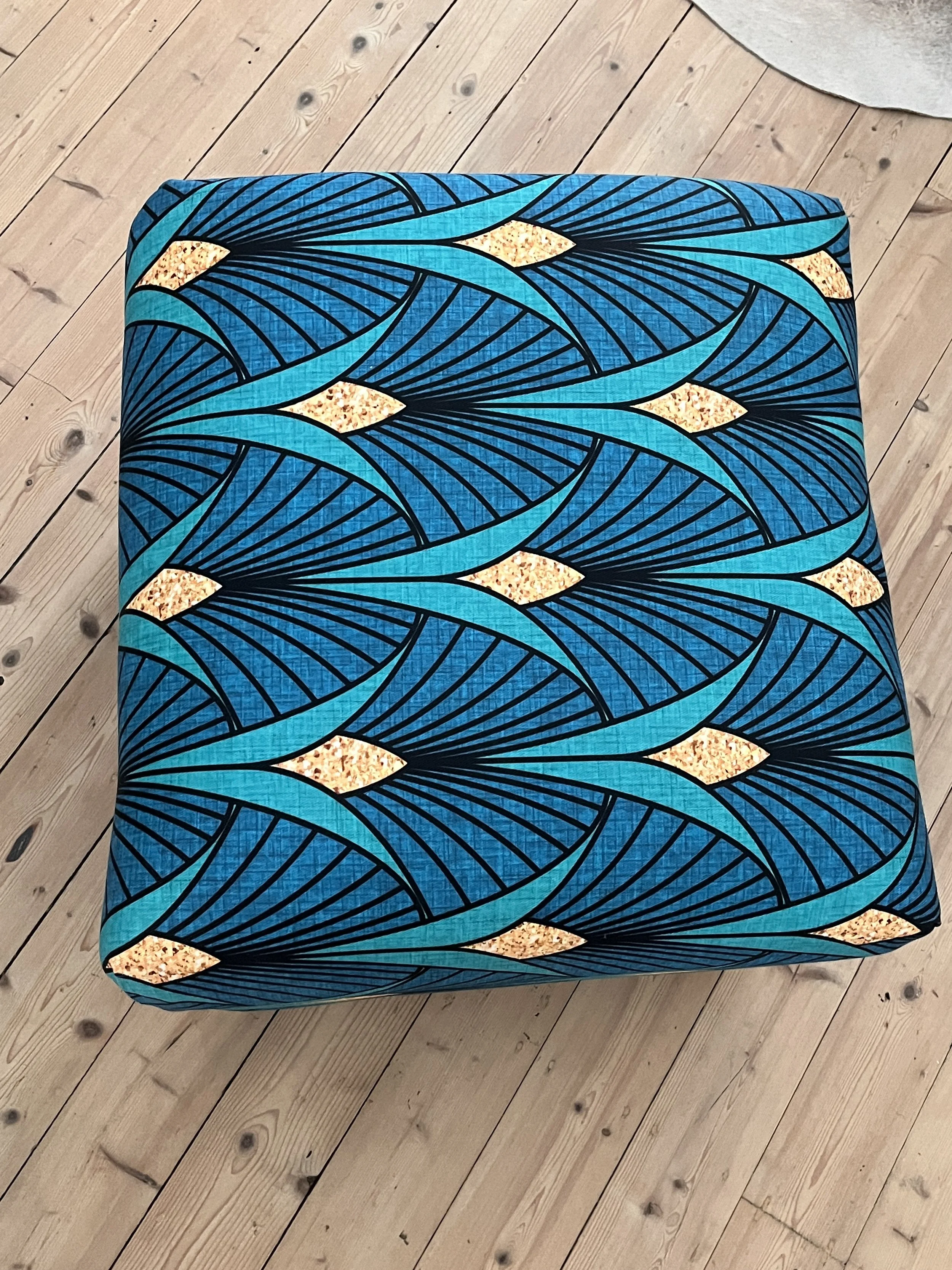 Blue and turquoise patterned fabric on a stool with a wooden floor background.