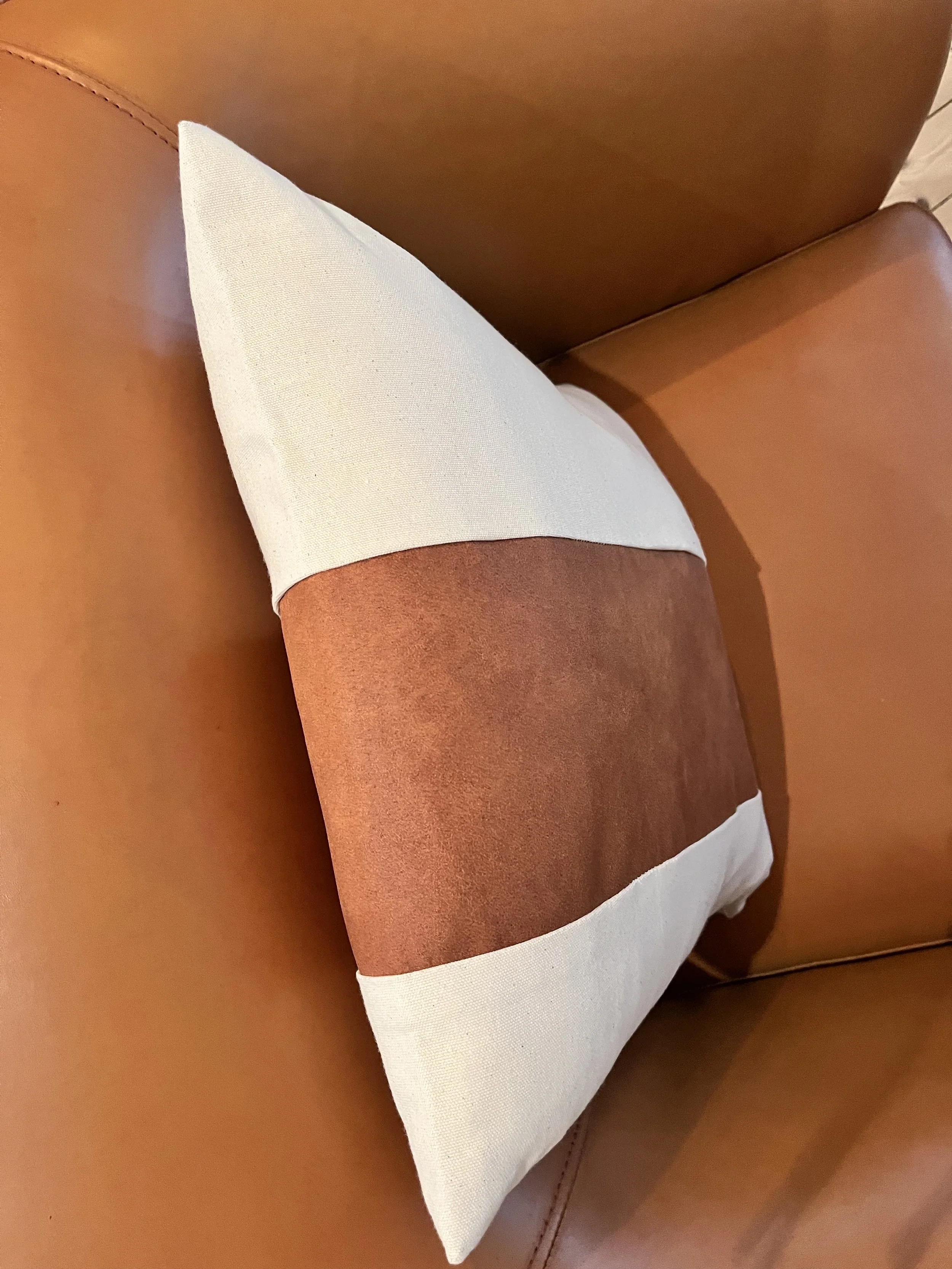 Square cushion with a white and brown stripe design on a brown leather chair.
