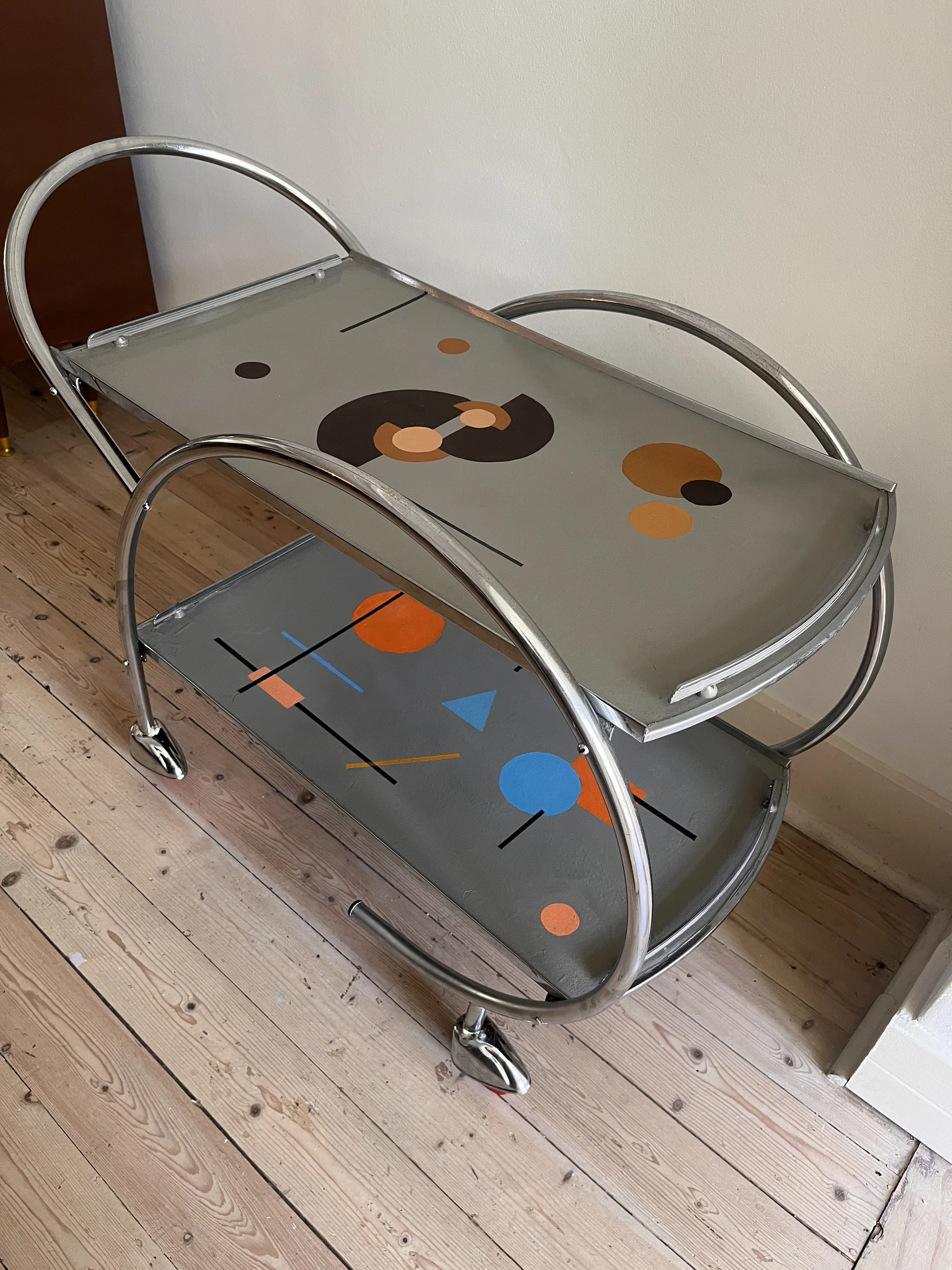 A modern metal bar cart with artistic geometric patterns on its surfaces, featuring wheels and curved handles.