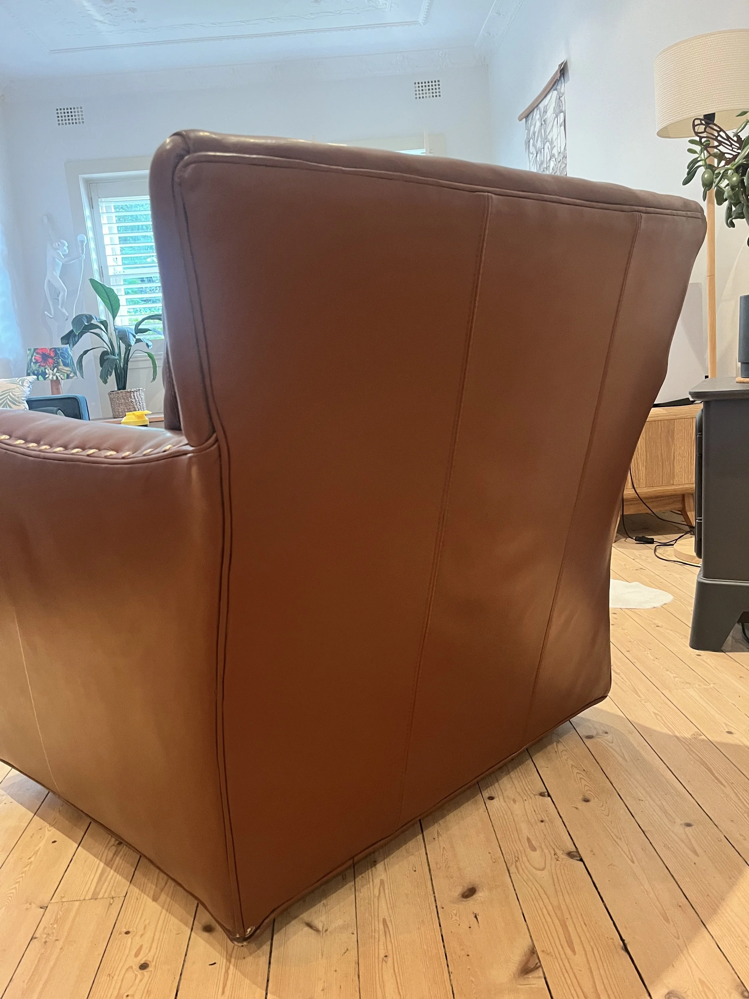 Brown leather armchair in a living room with wooden floor and indoor plants in the background.