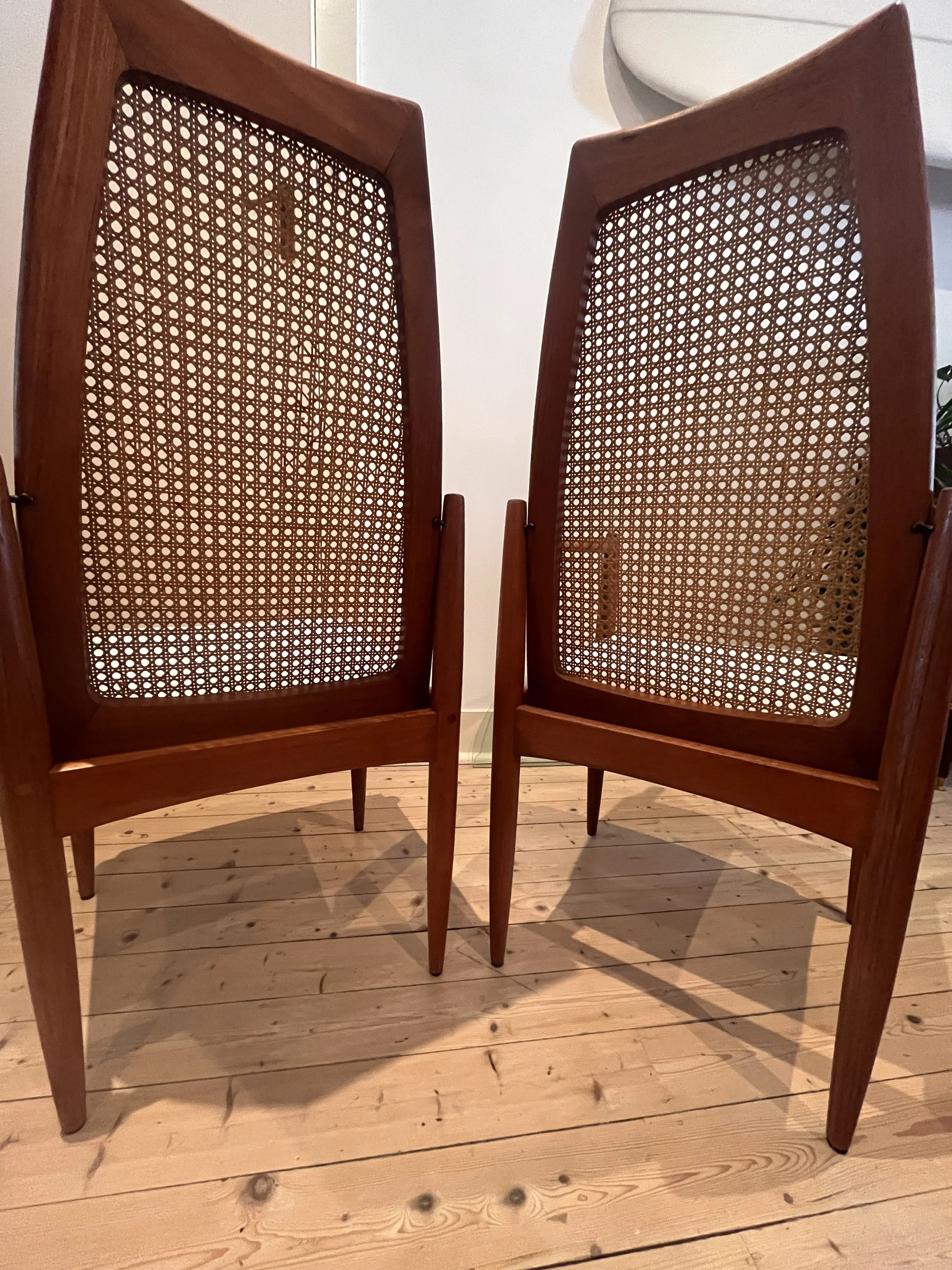 Two mid-century modern dining chairs with wooden frames and woven cane backs on a wooden floor.