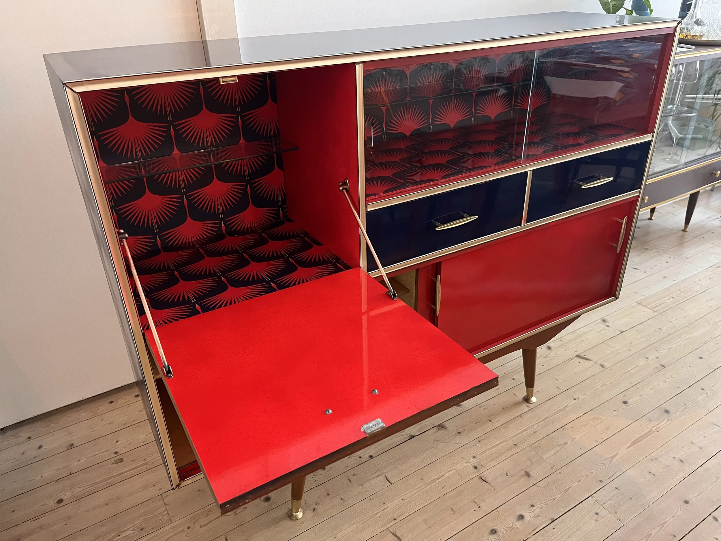 Vintage mid-century modern cabinet with red and black geometric design, featuring a drop-down door and multiple compartments.