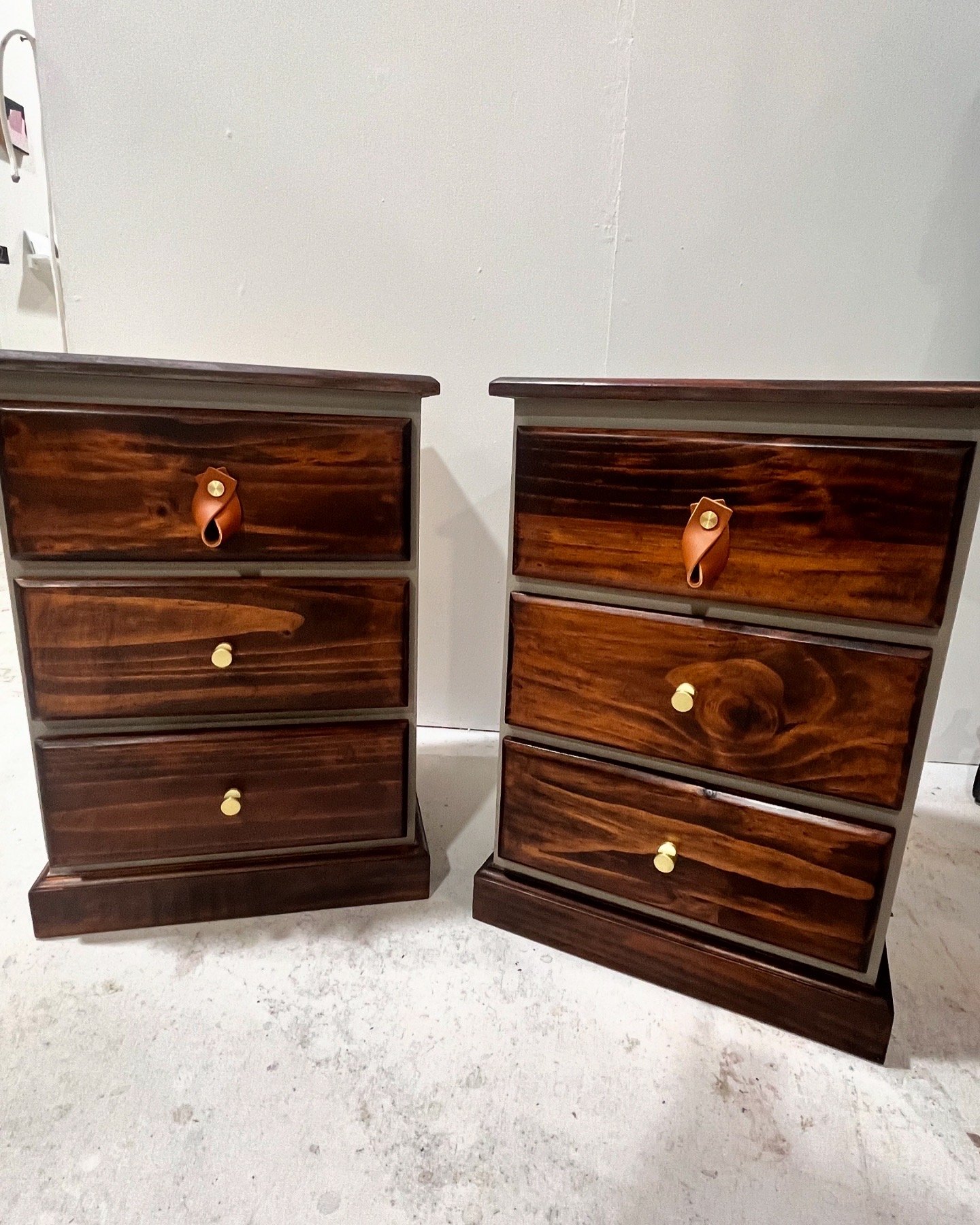 Two wooden nightstands with three drawers each, featuring dark wood finish and golden knobs, placed against a light wall on a concrete floor.
