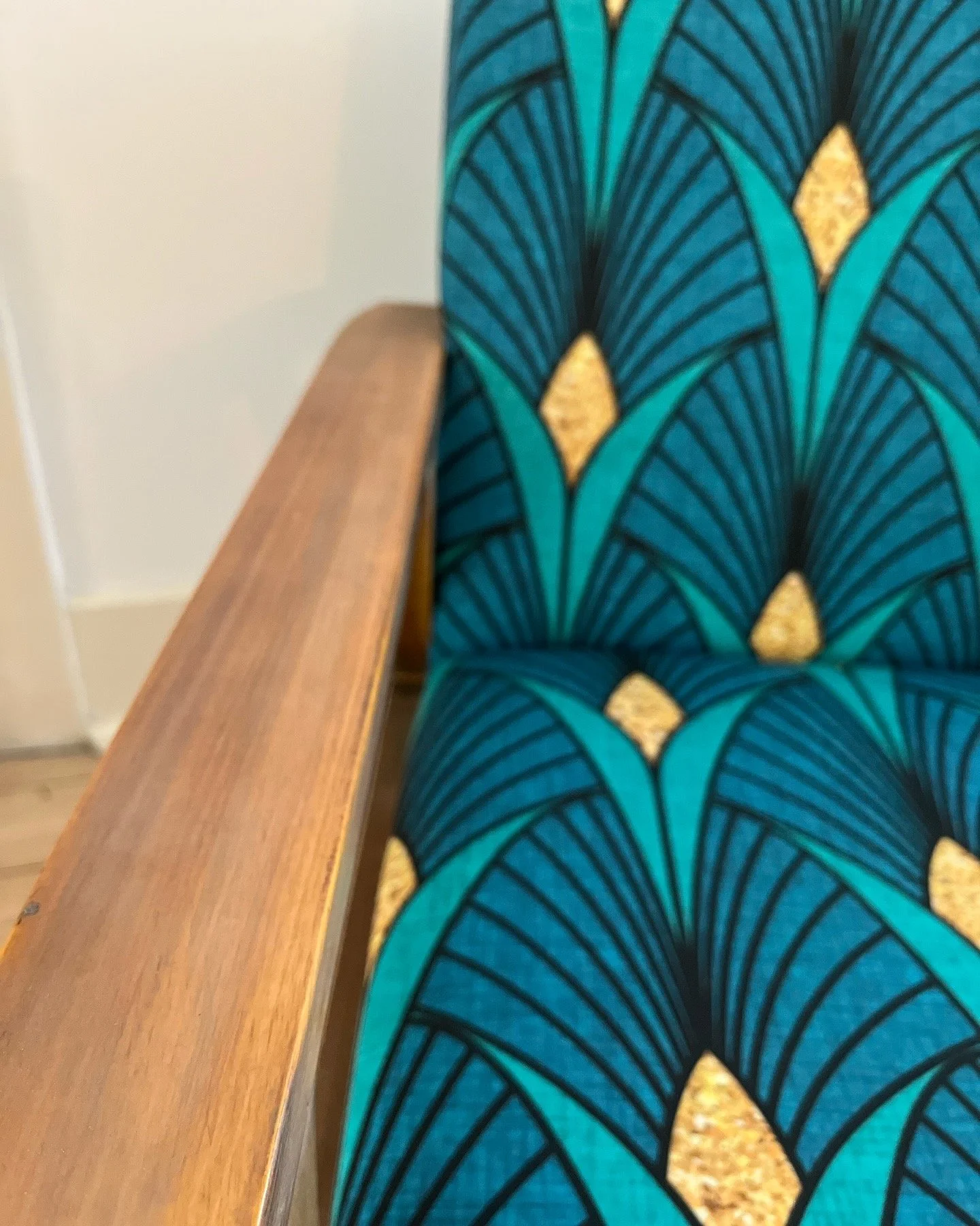Close-up of a chair with blue and green geometric upholstery and a wooden armrest.