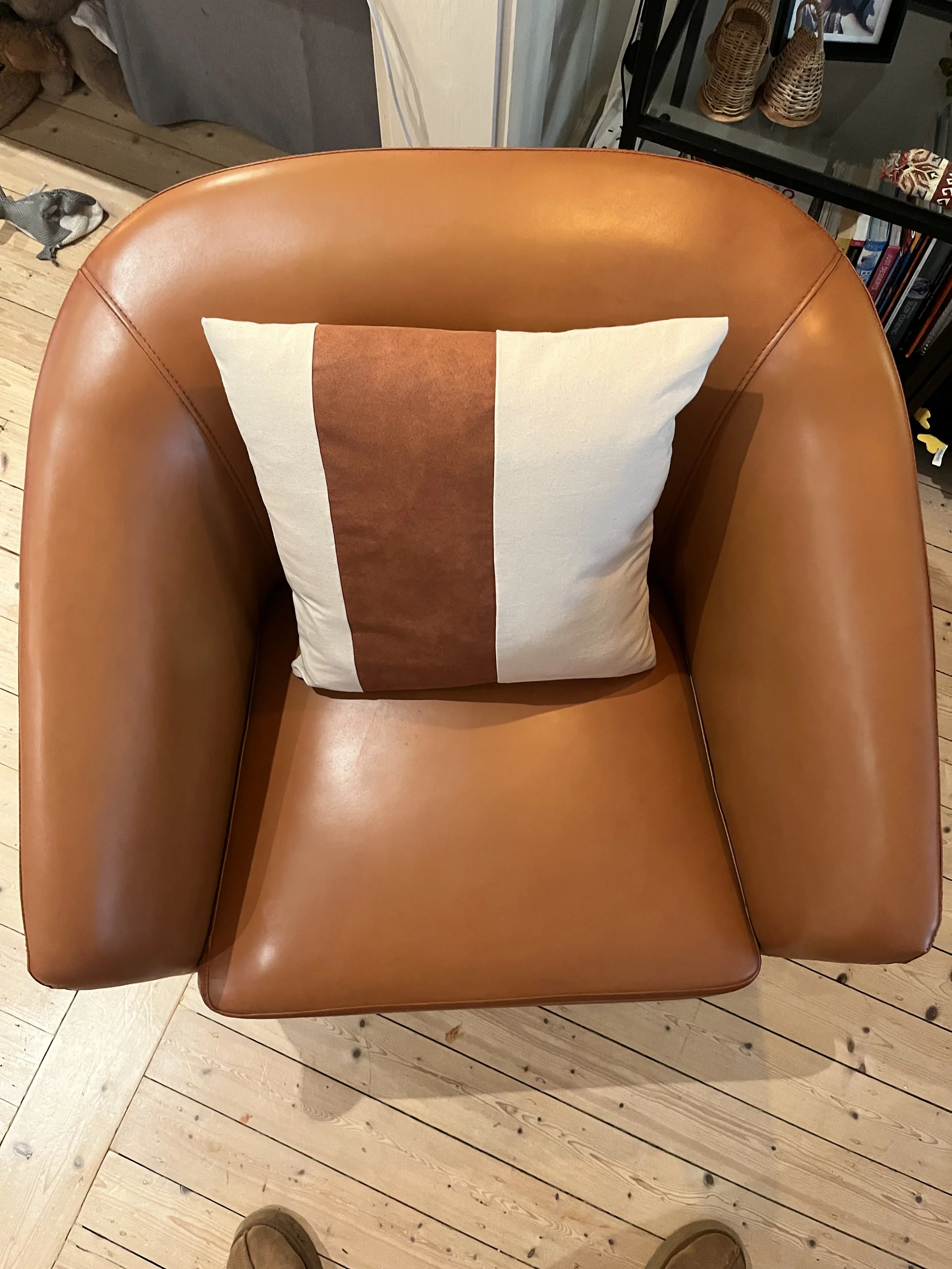 Brown leather chair with a white and brown pillow on a wooden floor.
