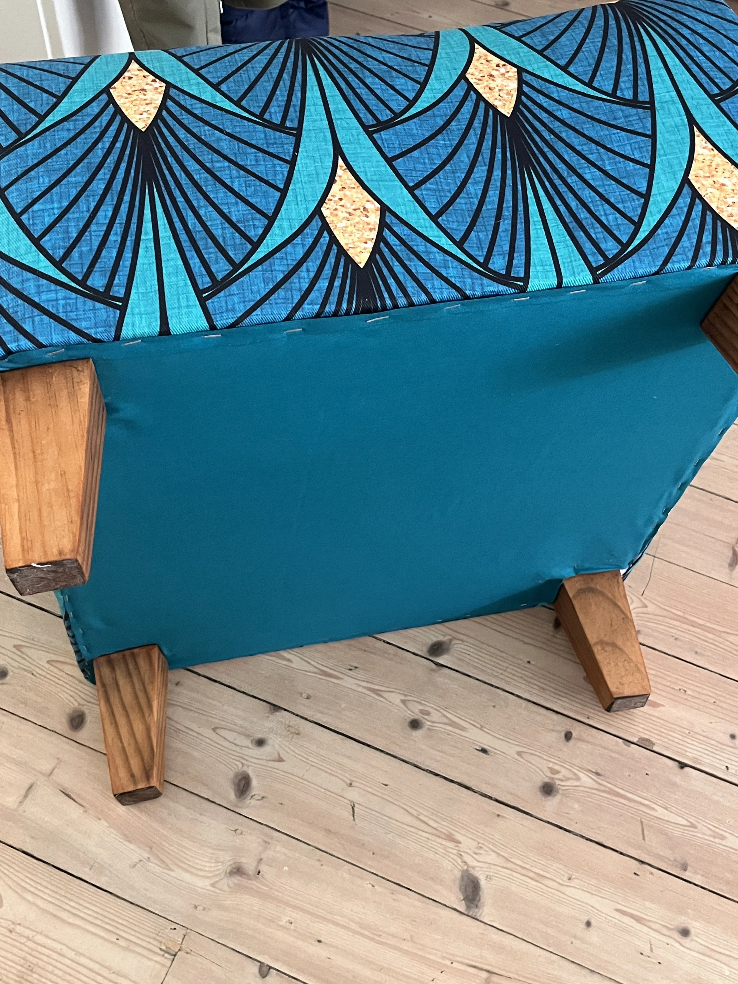 Upholstered bench with blue geometric fabric and wooden legs on a wooden floor.
