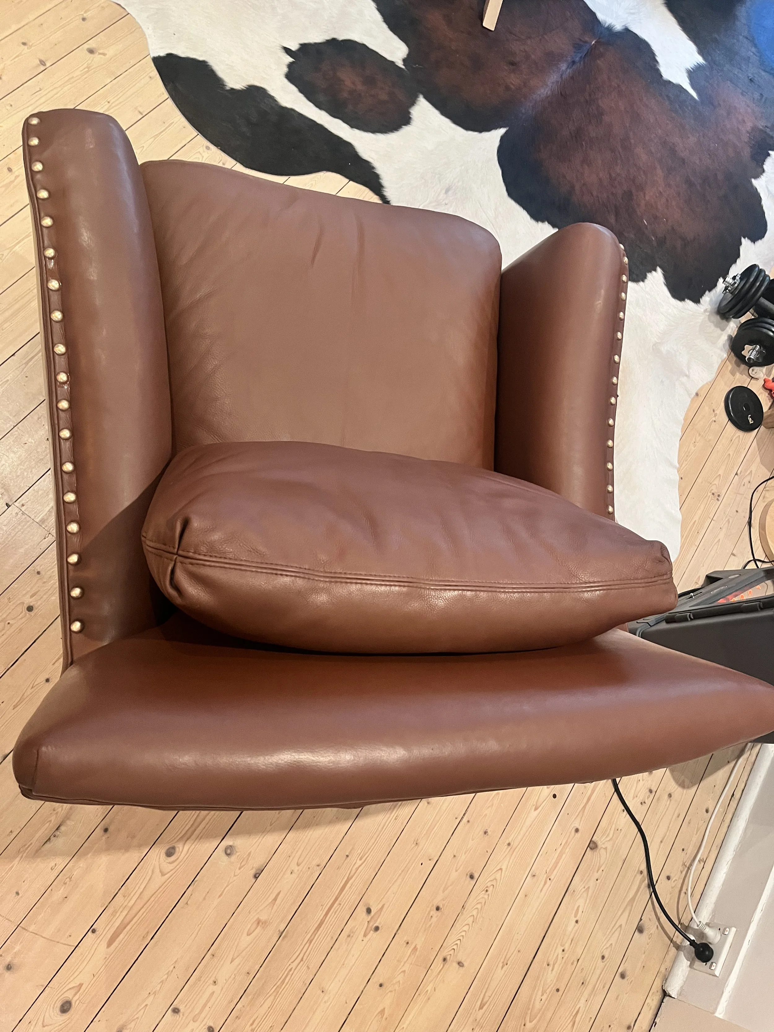 Top view of a brown leather armchair with metal studs, placed on a wooden floor, with a black and white cowhide rug partially visible beneath it.