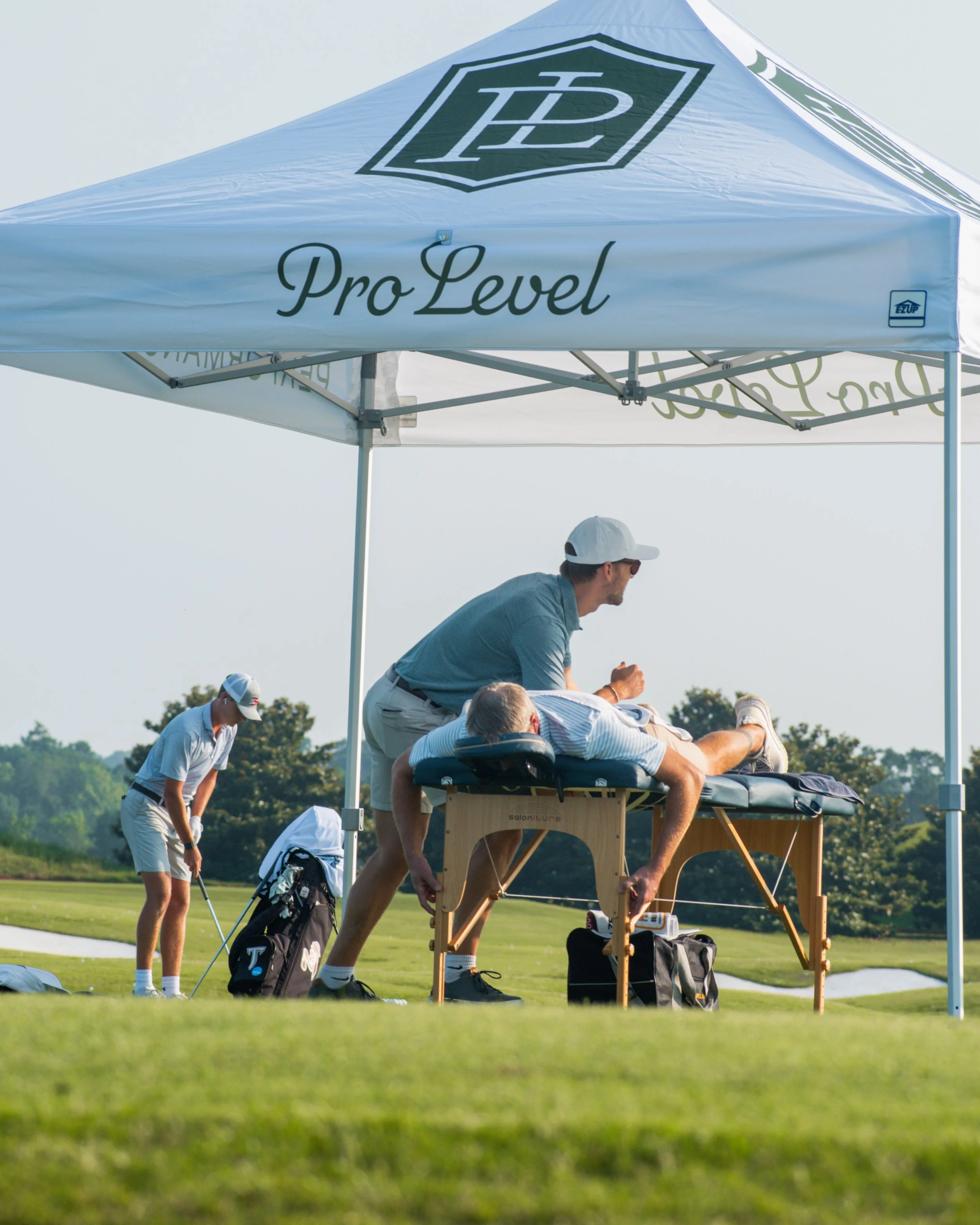 A golf statistician or trainer is measuring a golfer's swing underneath a tent with 'Pro Level' written on it, on a golf course.