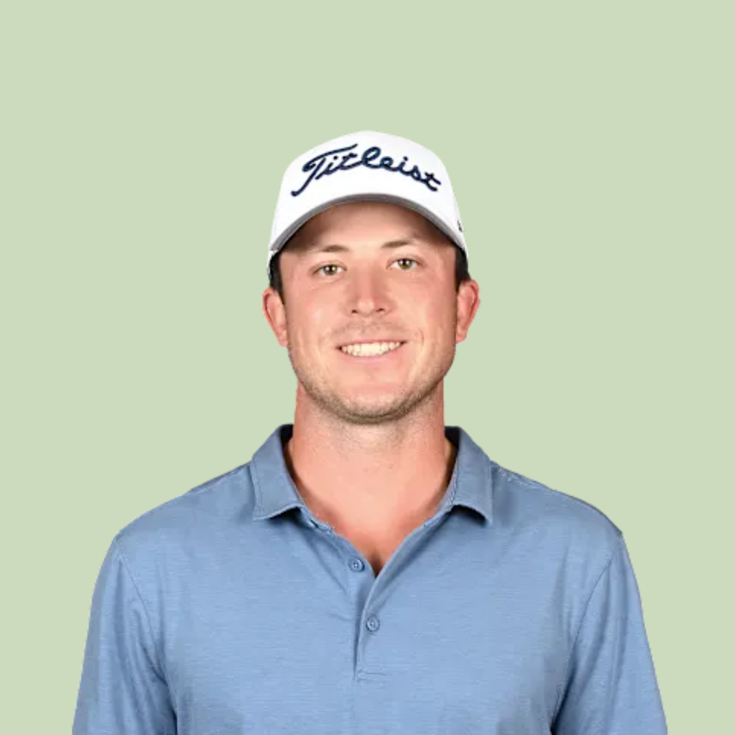 Close-up of a young man wearing a light blue collared shirt and a white cap with the Titleist logo on it, smiling against a light green background.