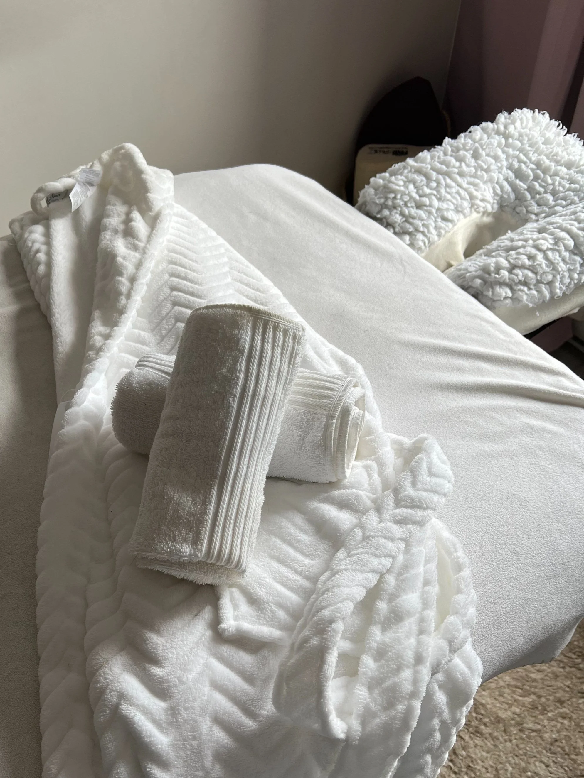 Spa or massage bed with white towels, a plush robe, and a fluffy neck pillow.
