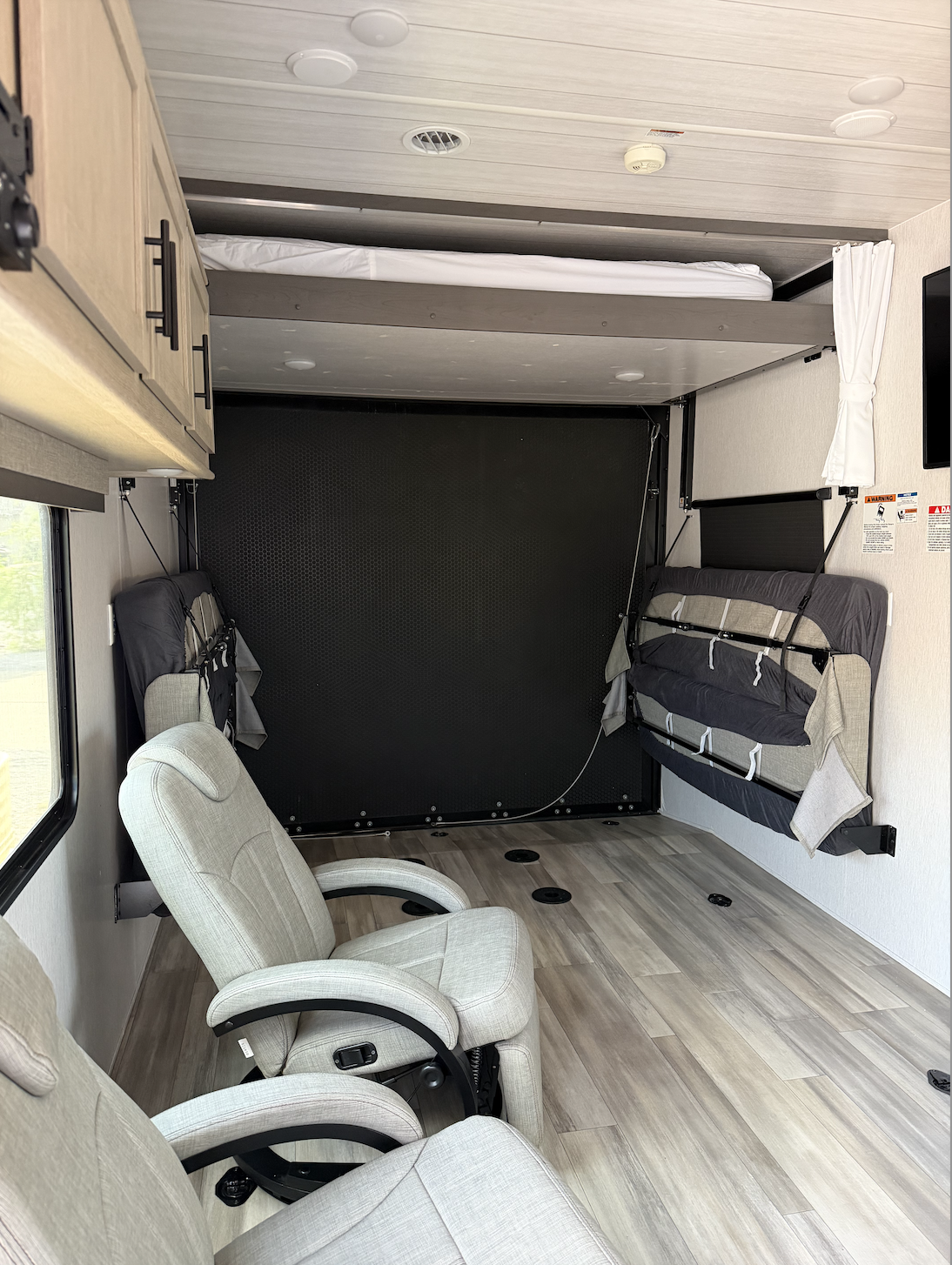 Interior of a camper with a raised bed, chairs, and storage compartments.