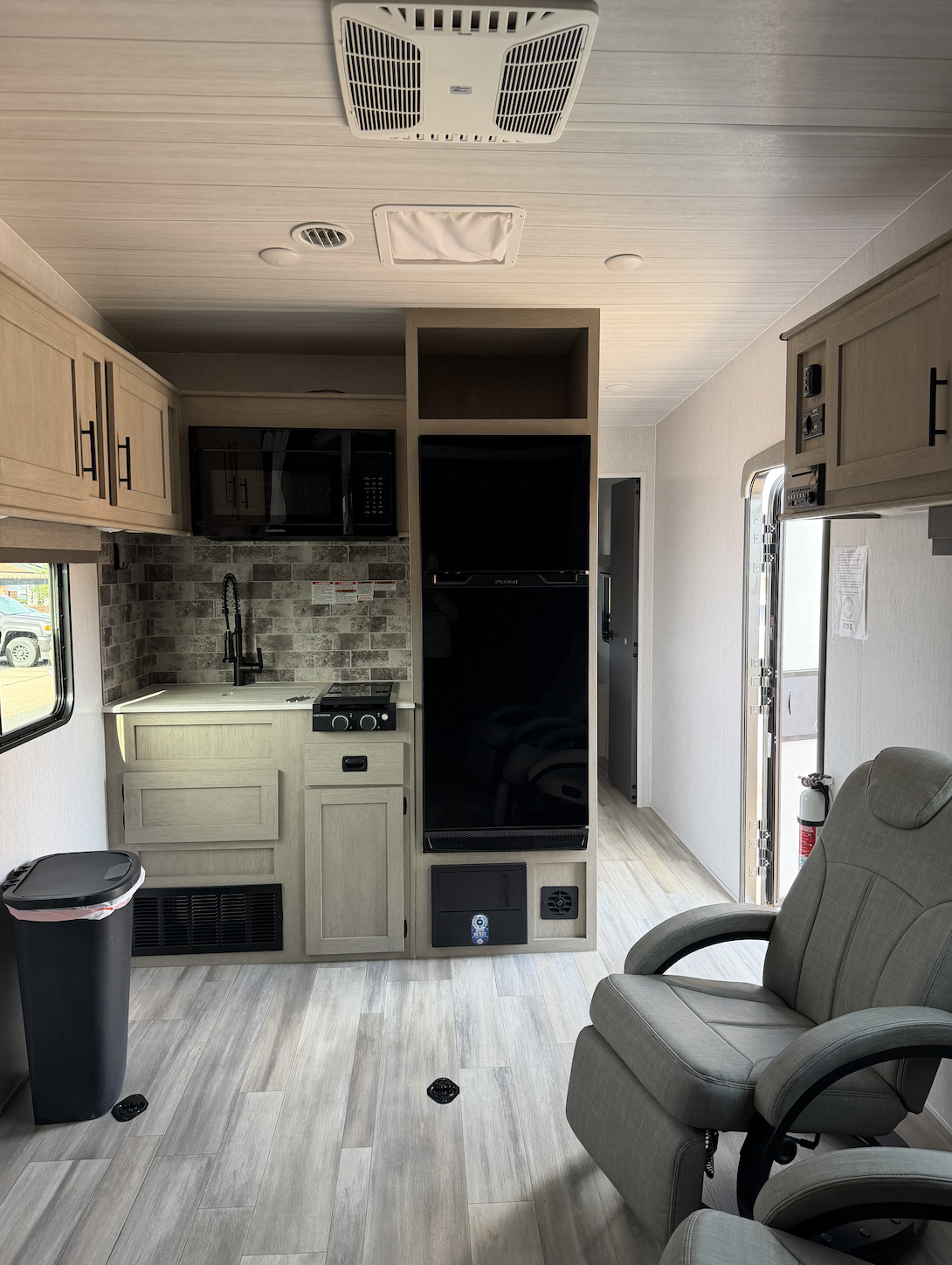 Interior of a compact RV or camper with a small kitchen, microwave, TV, and seating area.