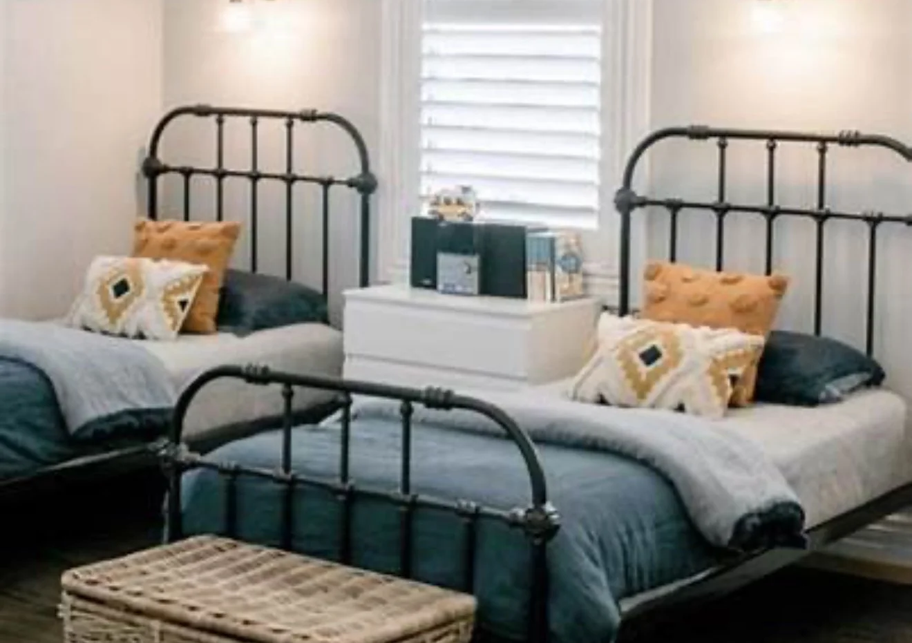 A bedroom with two metal-framed beds, a white dresser, decorative pillows, and a window with blinds.