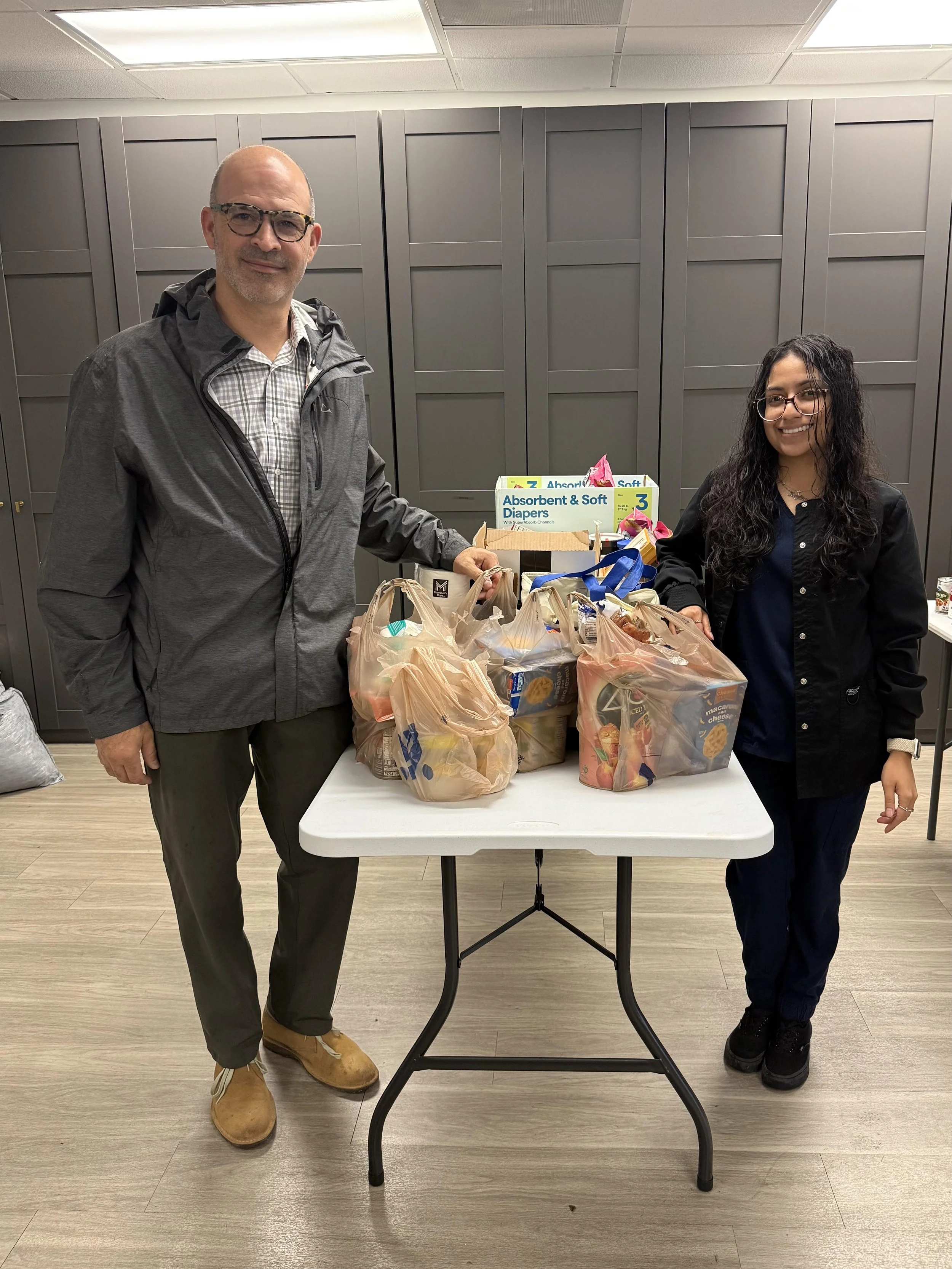 A man and a woman standing on either side of a table with bags of groceries on it.