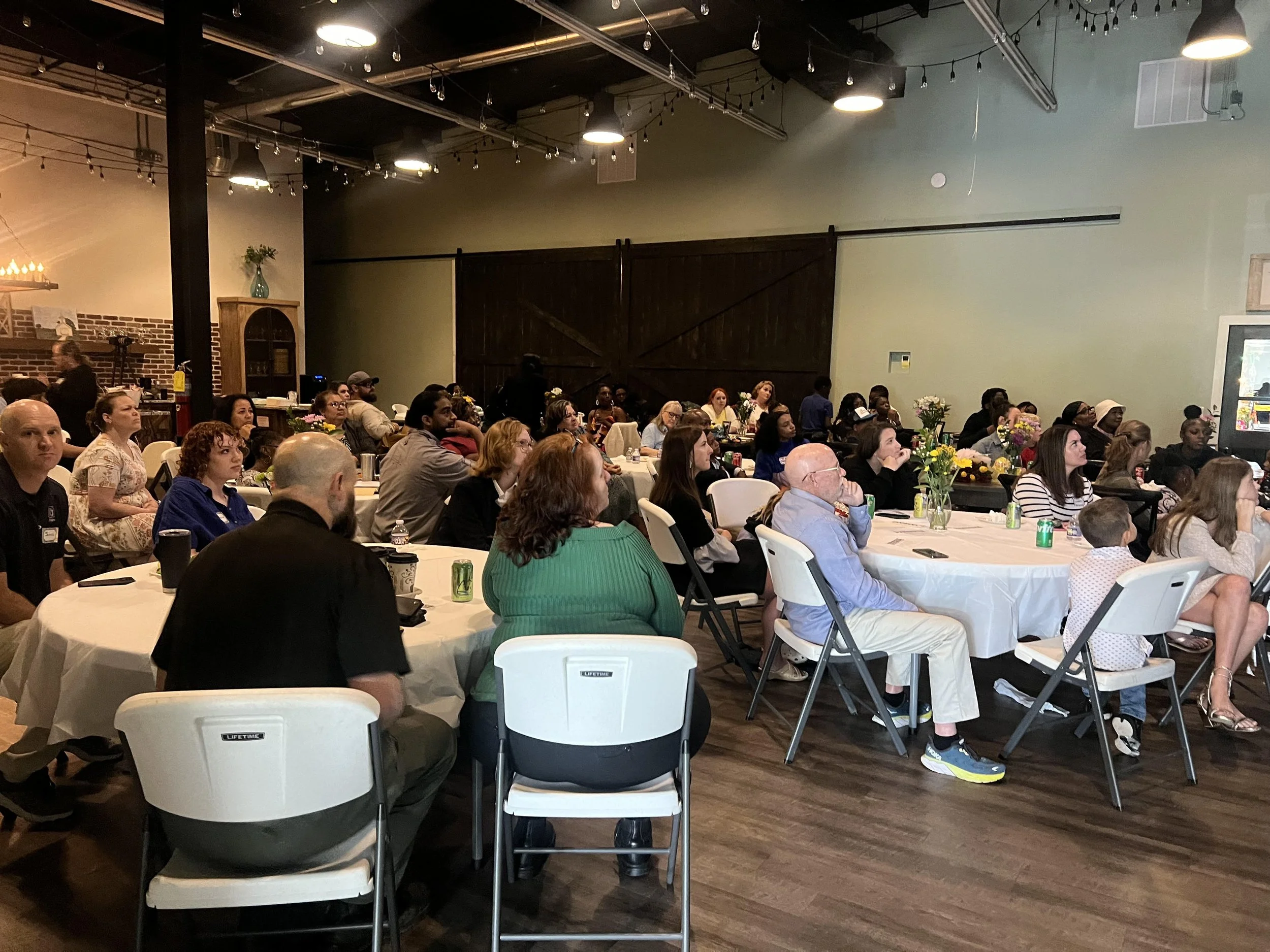 A large group of people sitting at various circular tables.