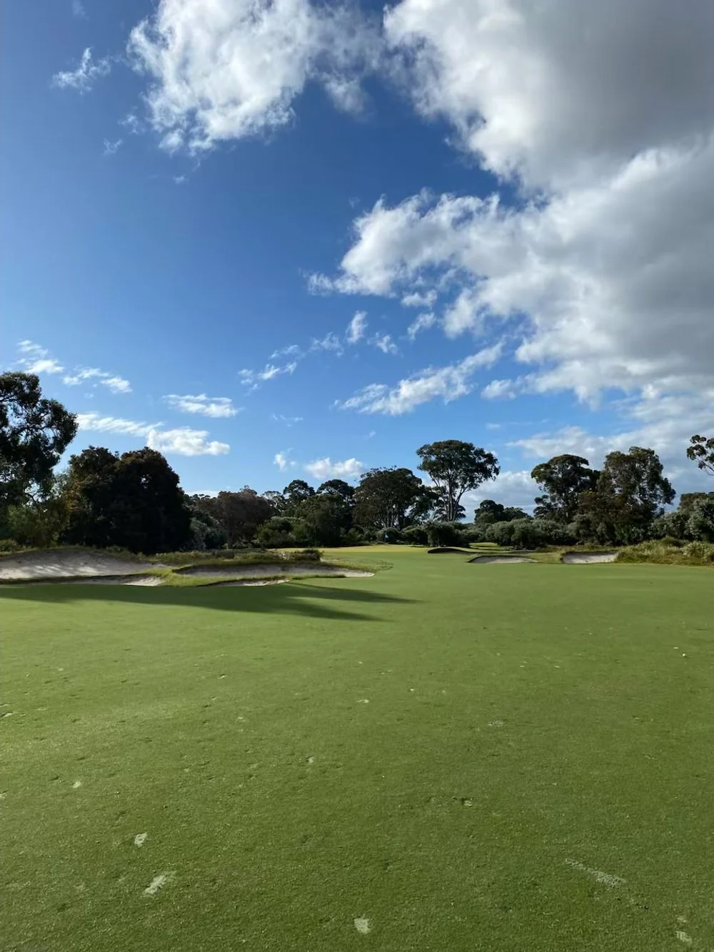 Golf course with green grass, sand traps, trees in the background, and a partly cloudy sky.
