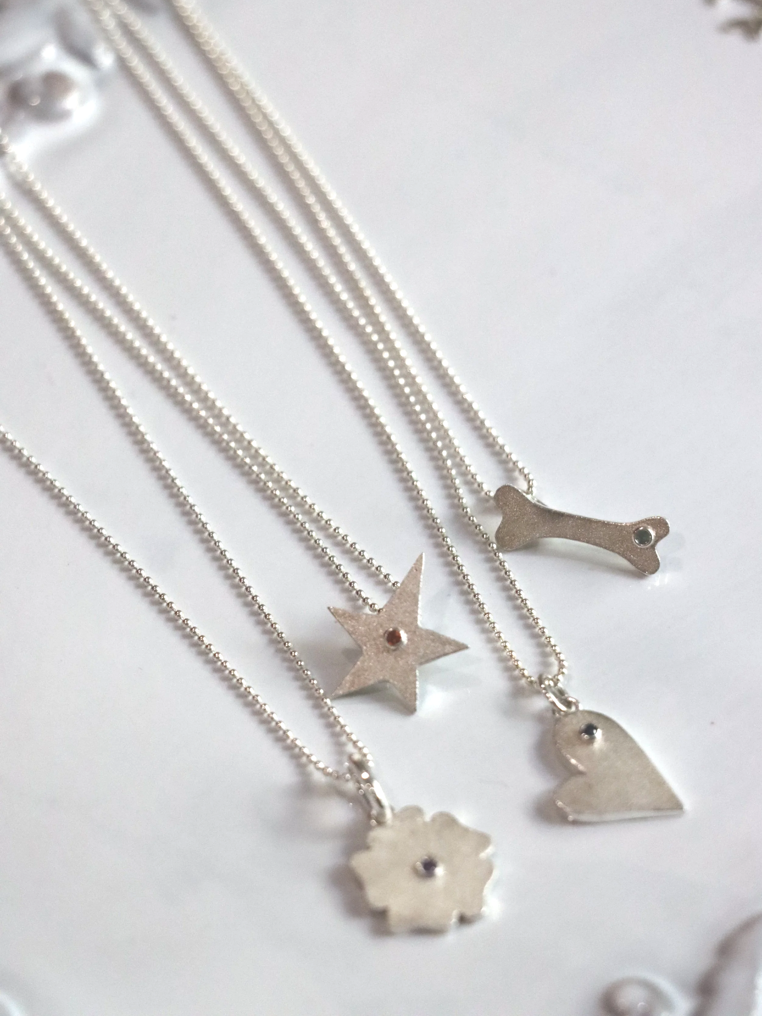 Close-up of a fluffy Ragdoll cat with blue eyes, pink nose, and a heart-shaped collar tag being touched under the chin.