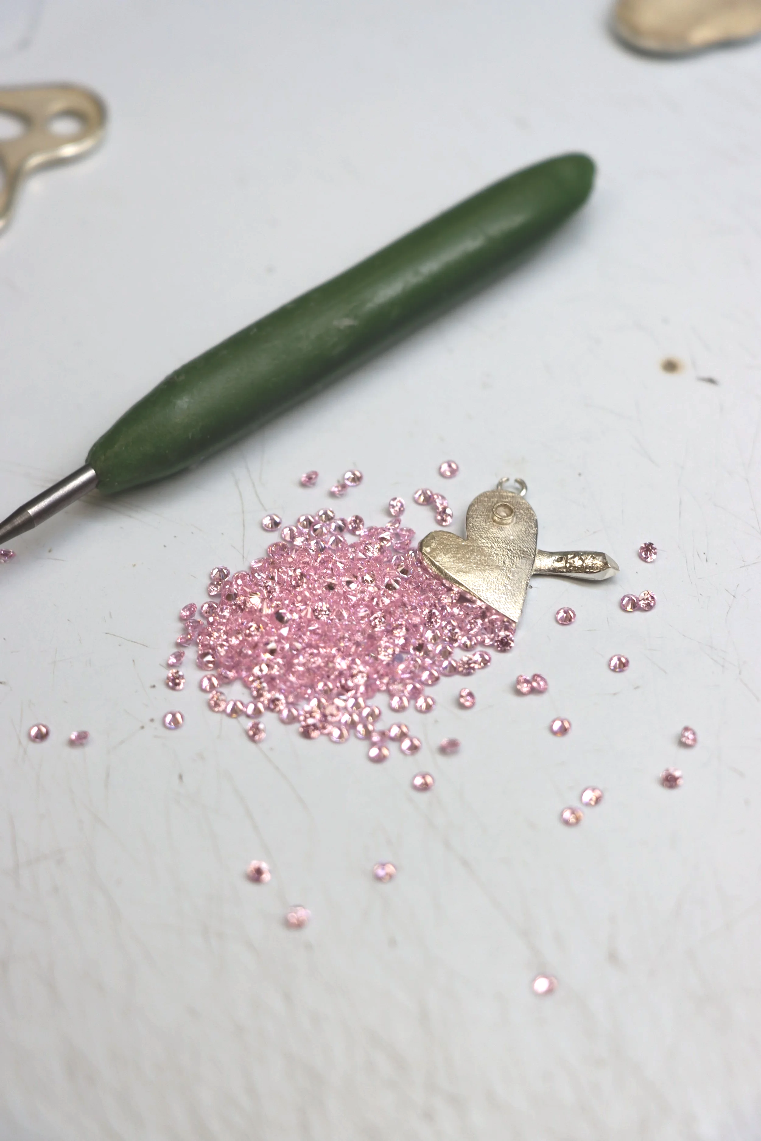 Small pile of purple gemstones or rhinestones on a white surface with a pair of tweezers in the background.
