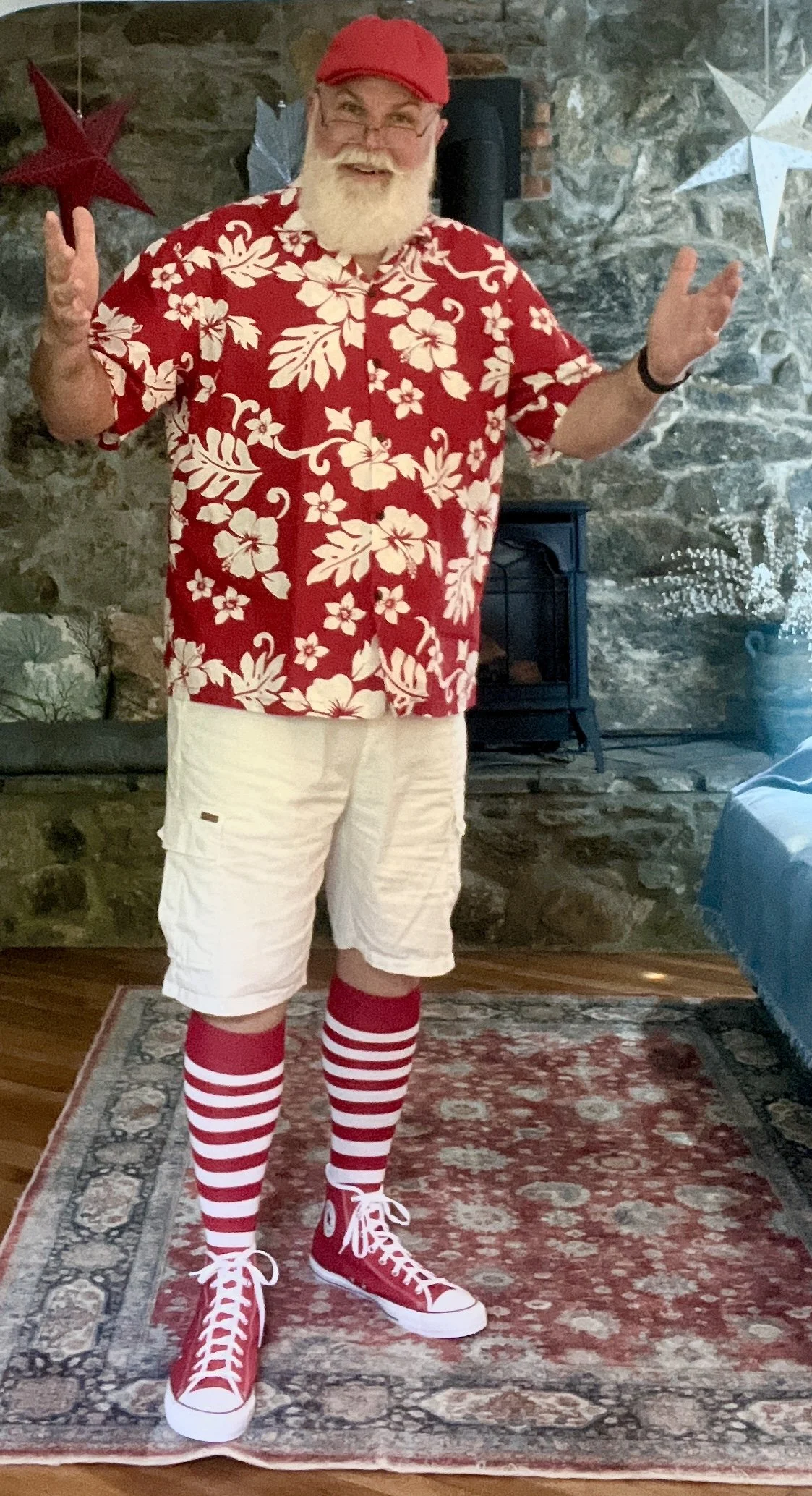 Man in festive outfit with red floral shirt, white shorts, red and white striped socks, and red sneakers.