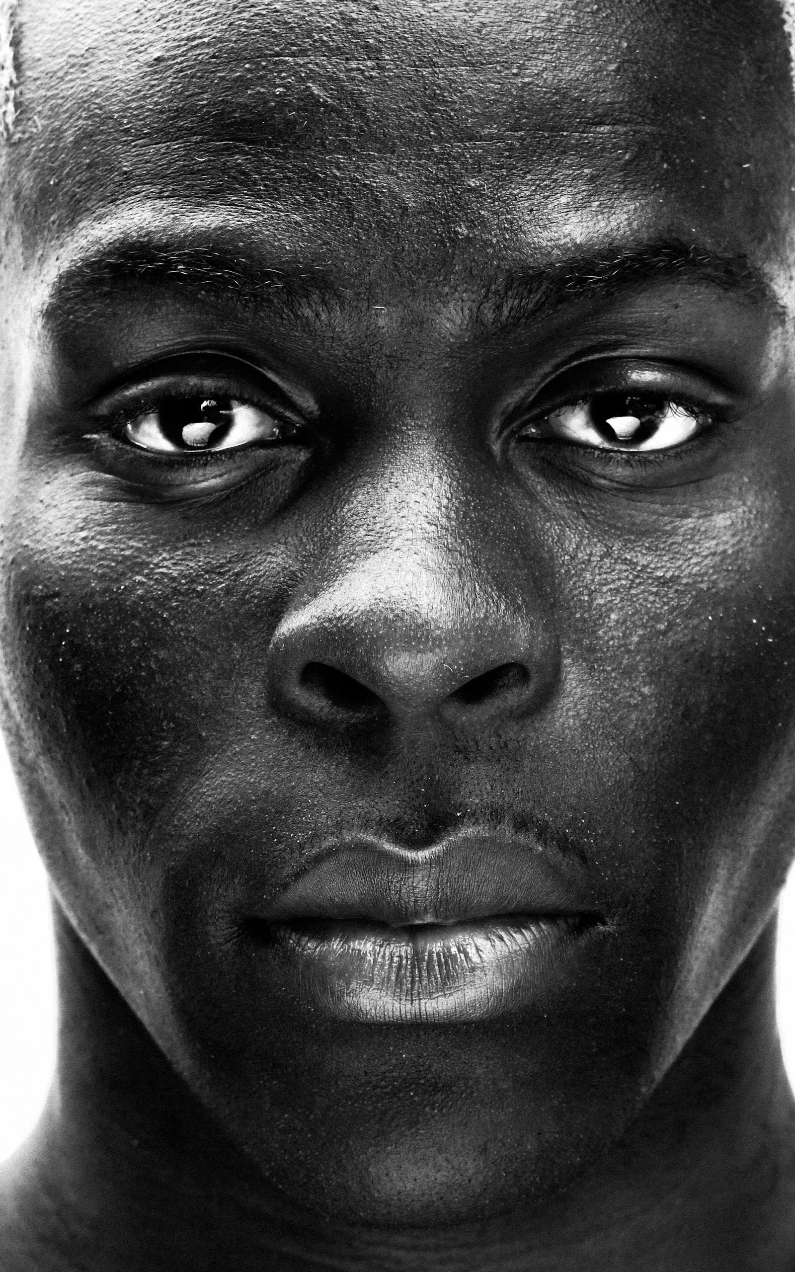 Close-up of a Black person's face in black and white, showing detailed skin texture, eyes slightly looking up, and relaxed lips.