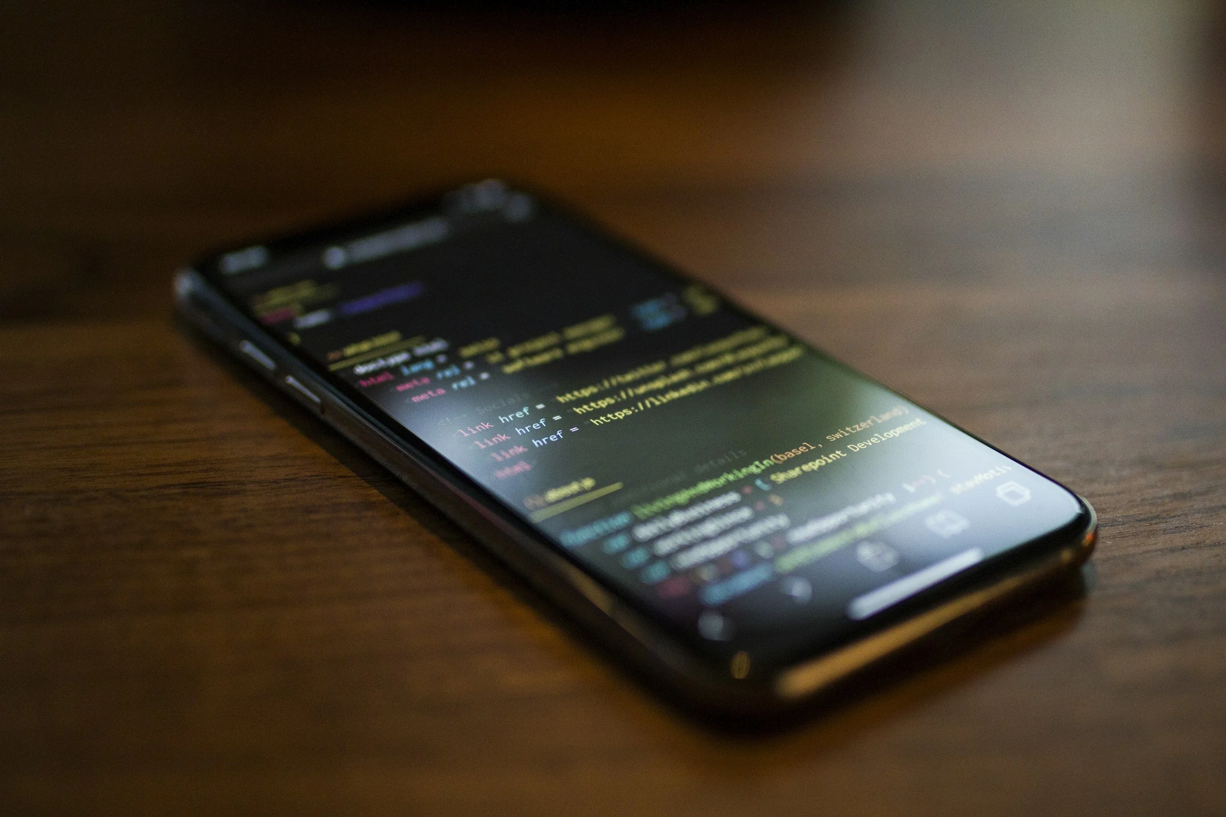 Smartphone on a wooden surface displaying lines of code or script, with the screen brightly lit in a dark environment.