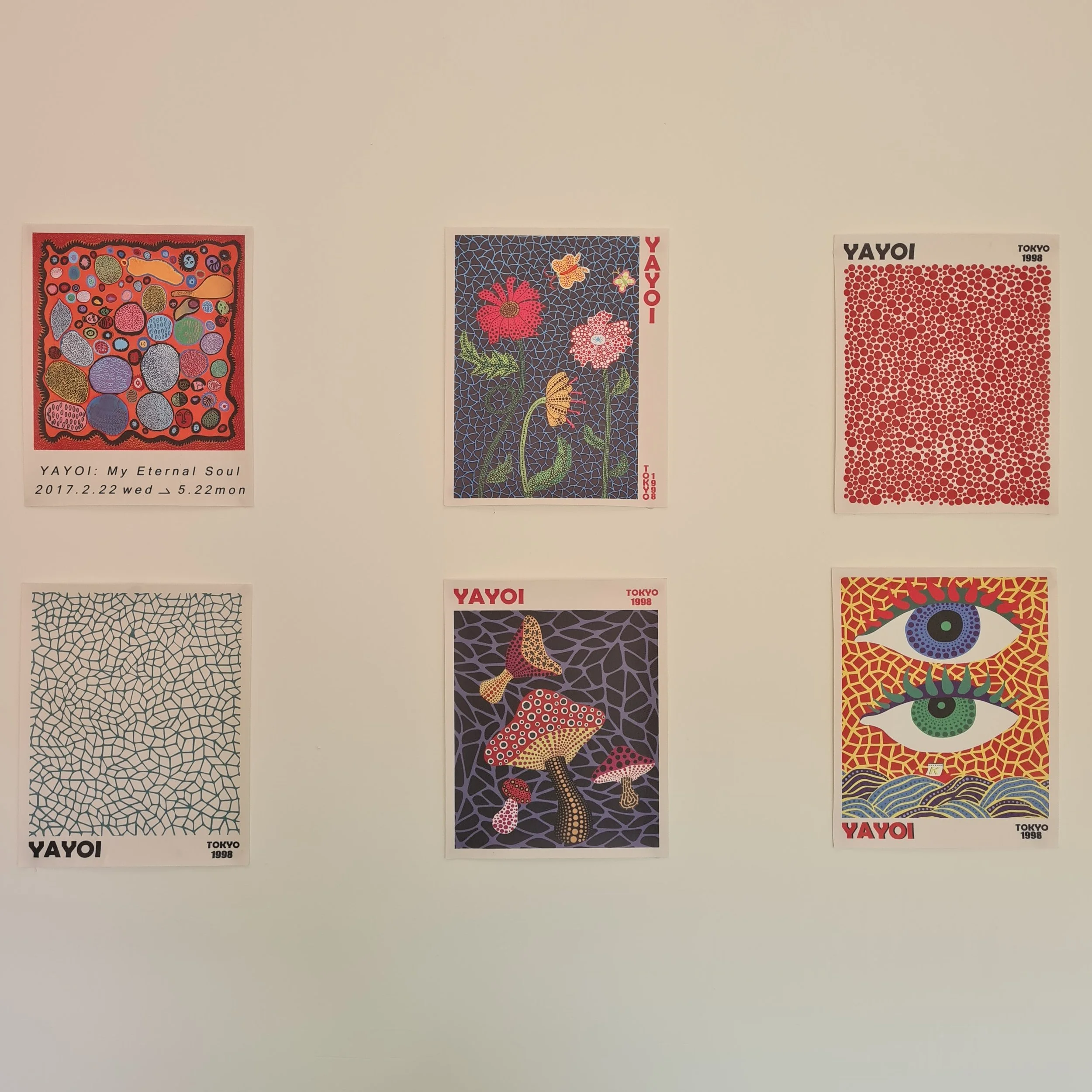 Six colorful posters with abstract and pop art designs on a white wall.