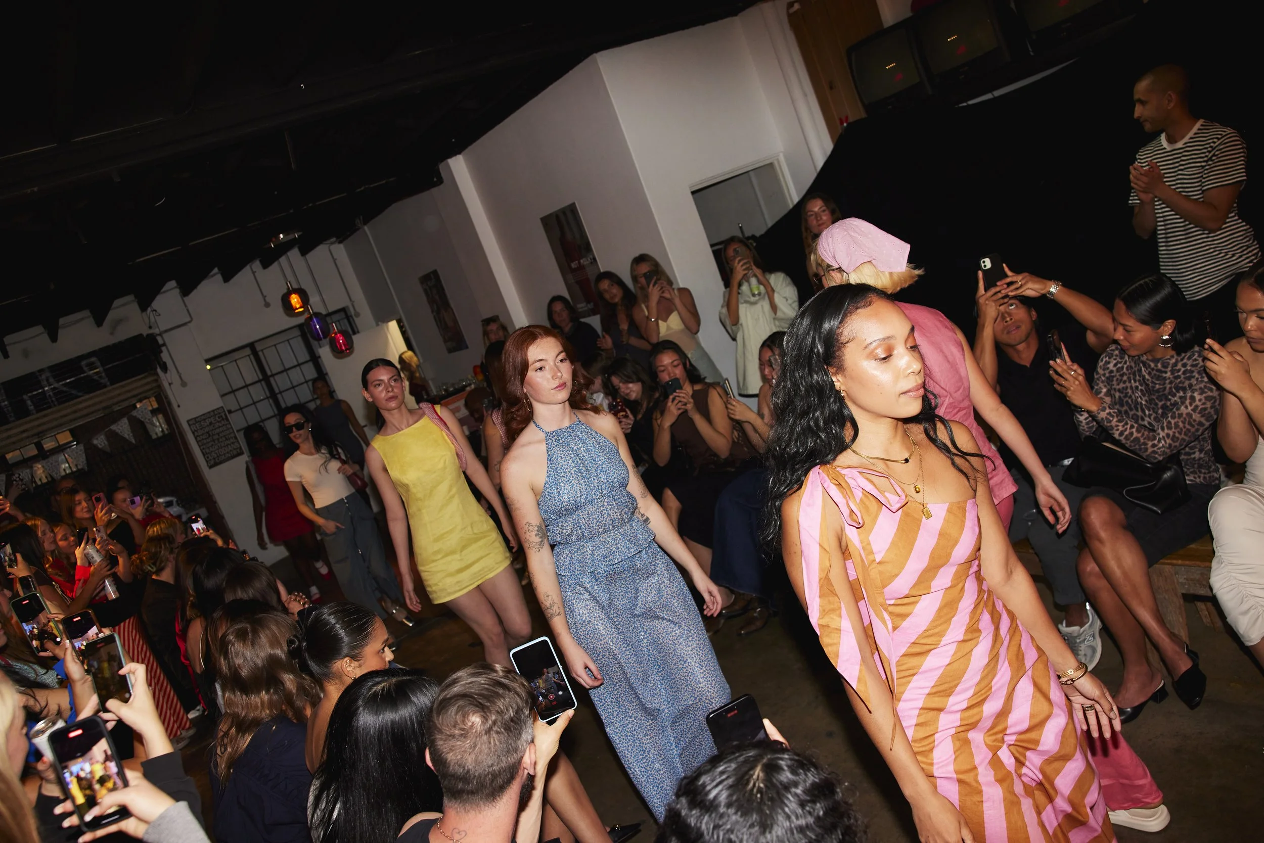 Models walking on a runway surrounded by seated audience at a fashion event.