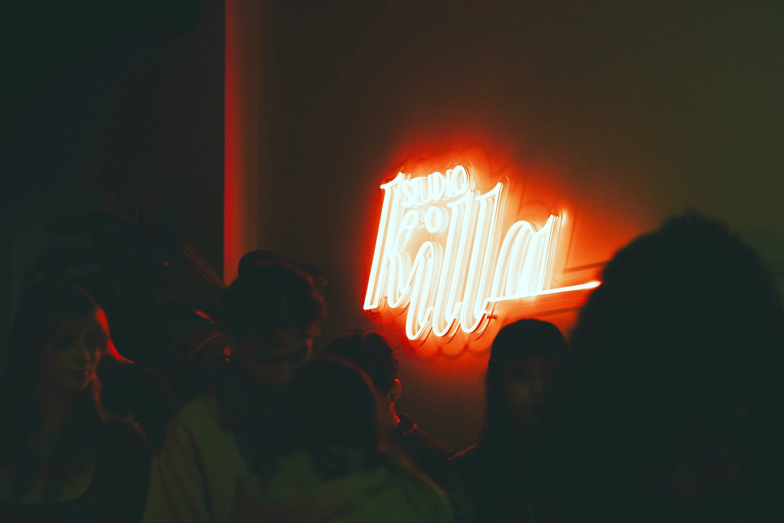 dimly lit room with neon sign 'Studio Killa' and people silhouettes