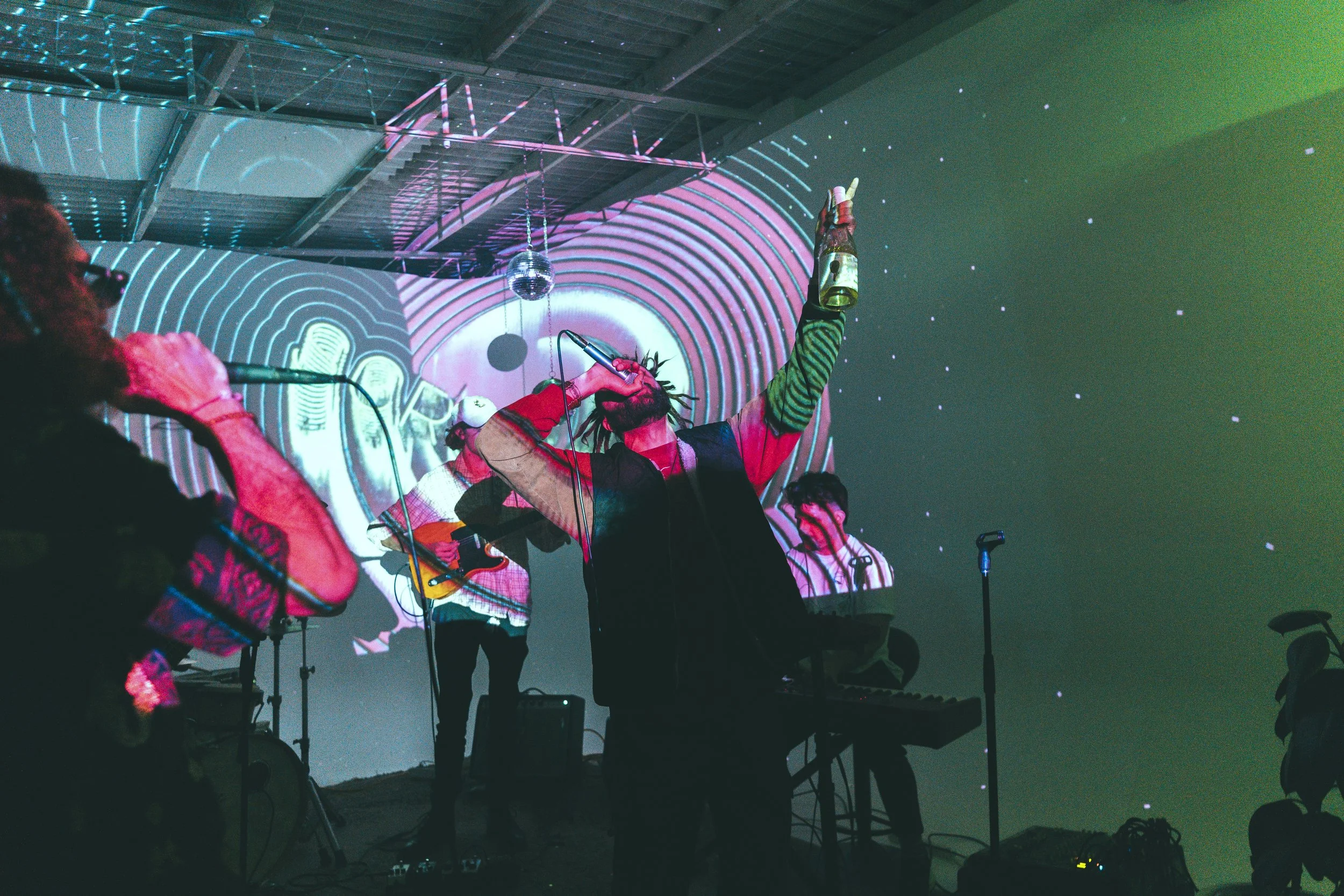 Live music performance with vibrant visual projections, musicians playing instruments and singing with microphones, colorful abstract background visuals