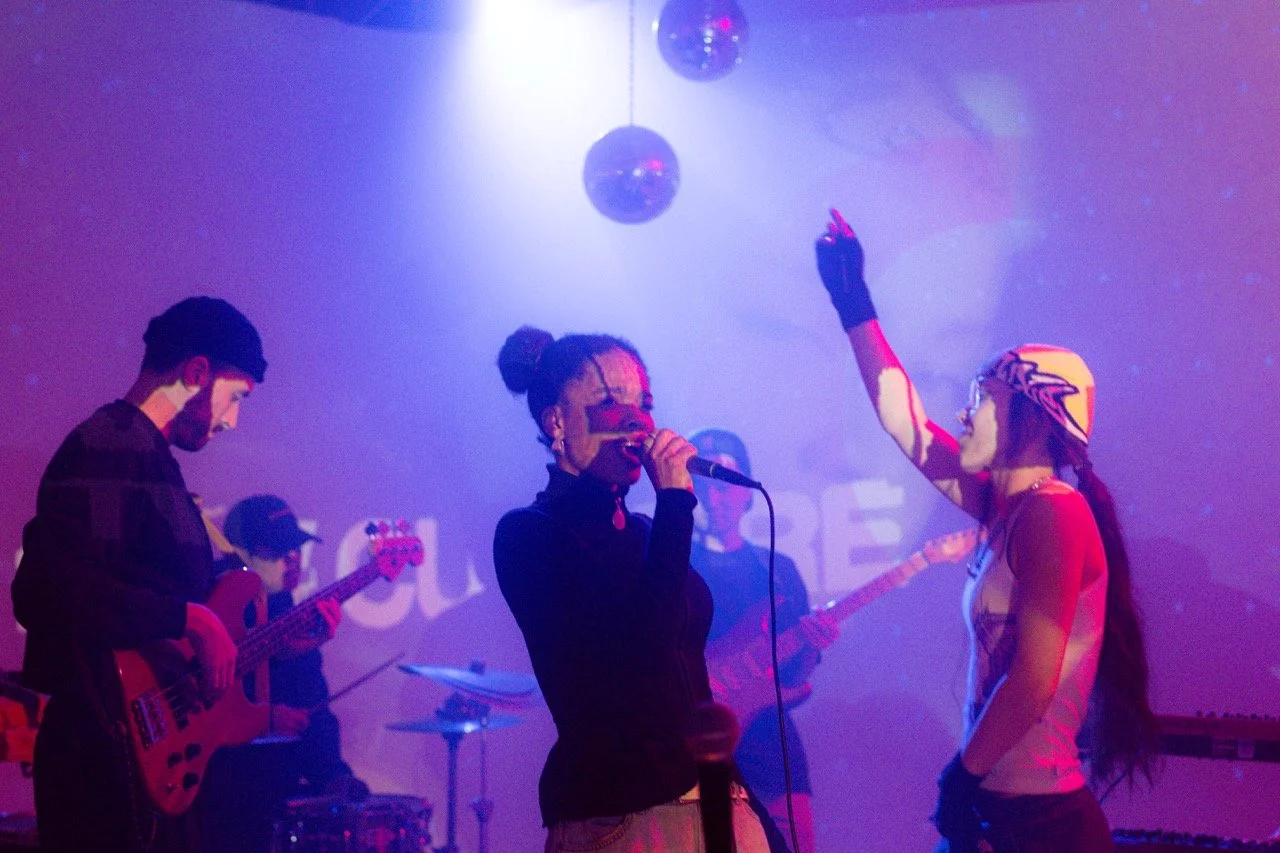 A band performing on stage with a vocalist and musicians playing guitars and drums under colorful lights.