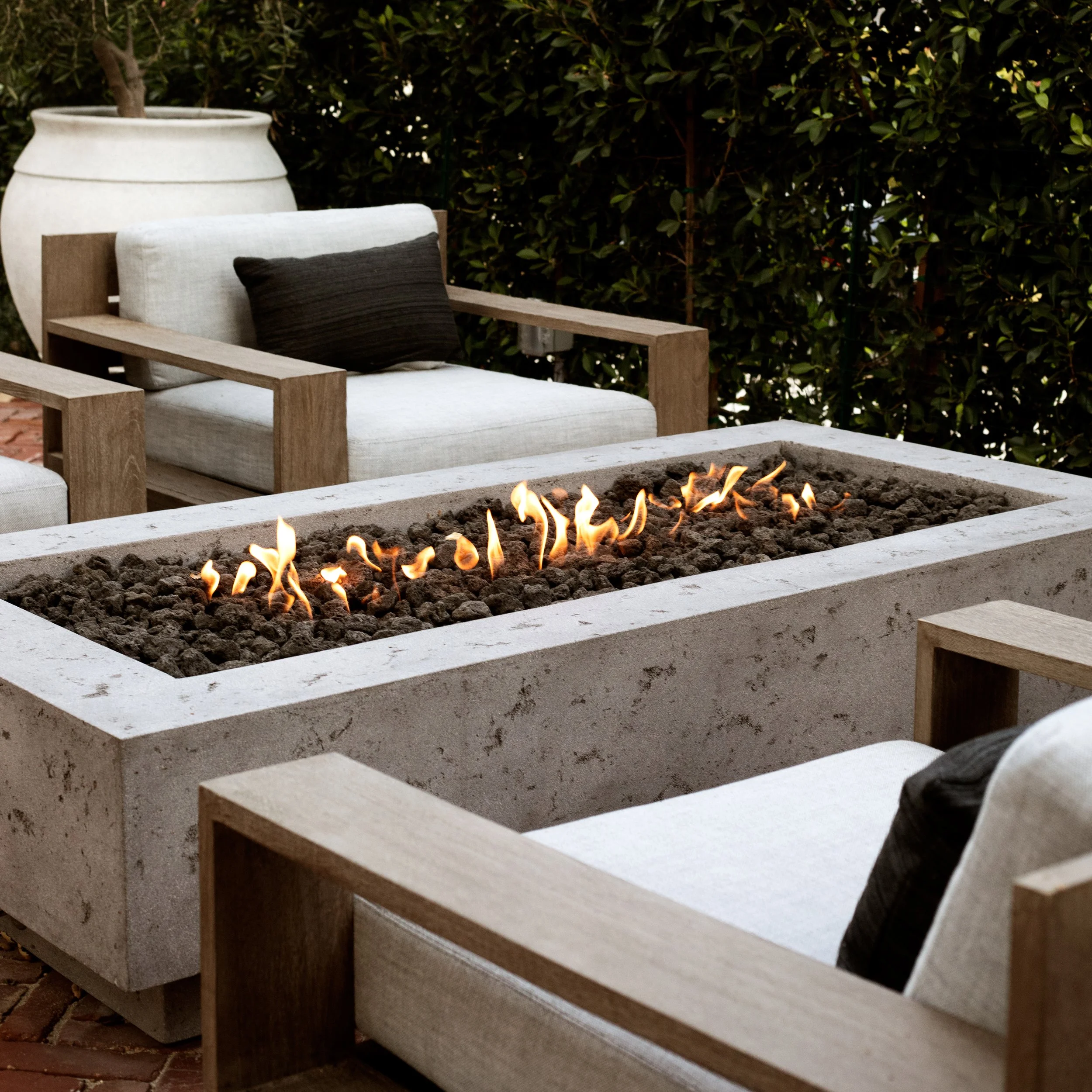 Elegant linear fire pit with relaxed lounge chairs and hedge background.