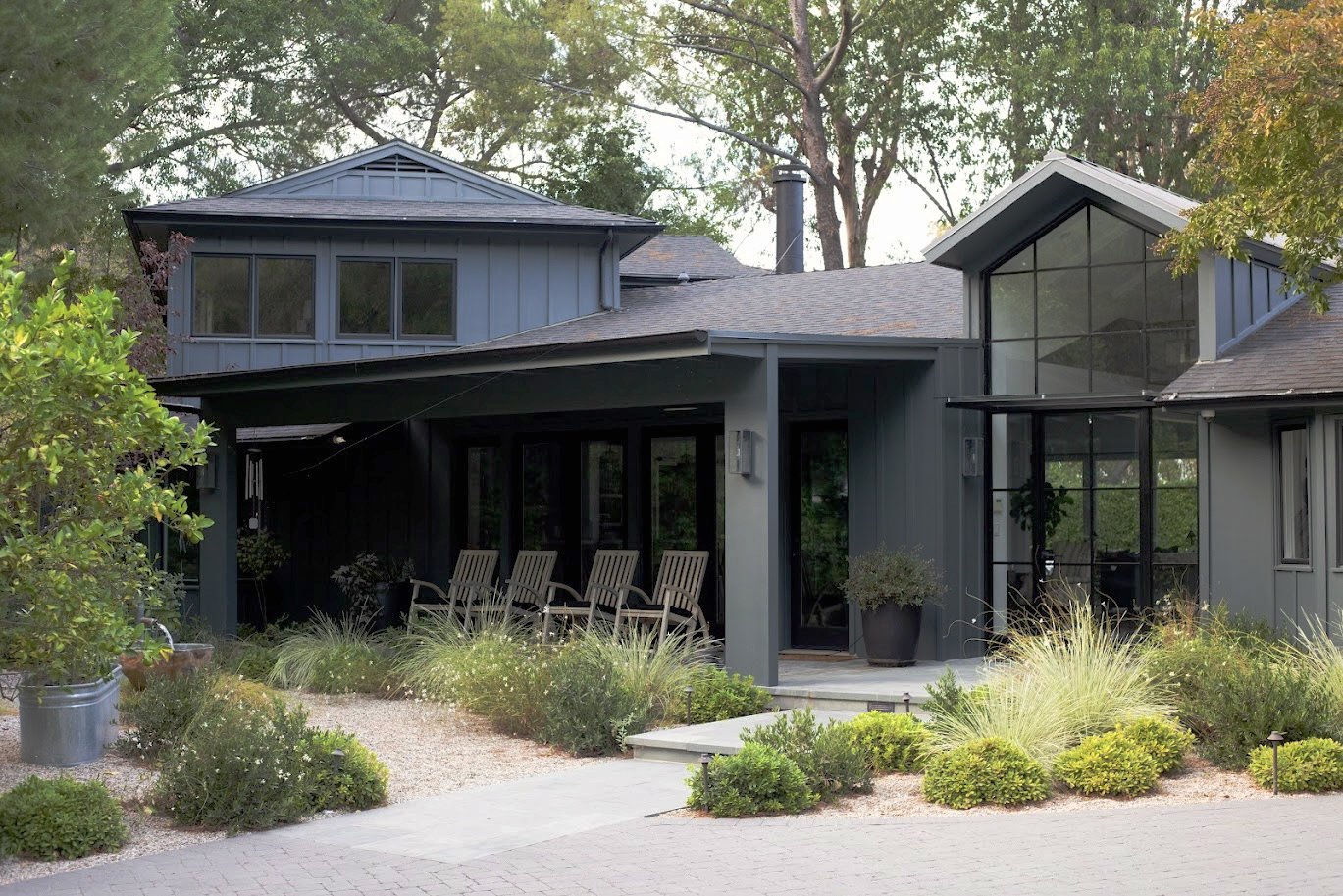 Large entertainer's yard with linear pool, chaise lounges, cantilevered umbrellas, fire pit gravel lounge, lush layered Mediterranean plantings and privacy hedges, front sitting porch, walkways through the garden.