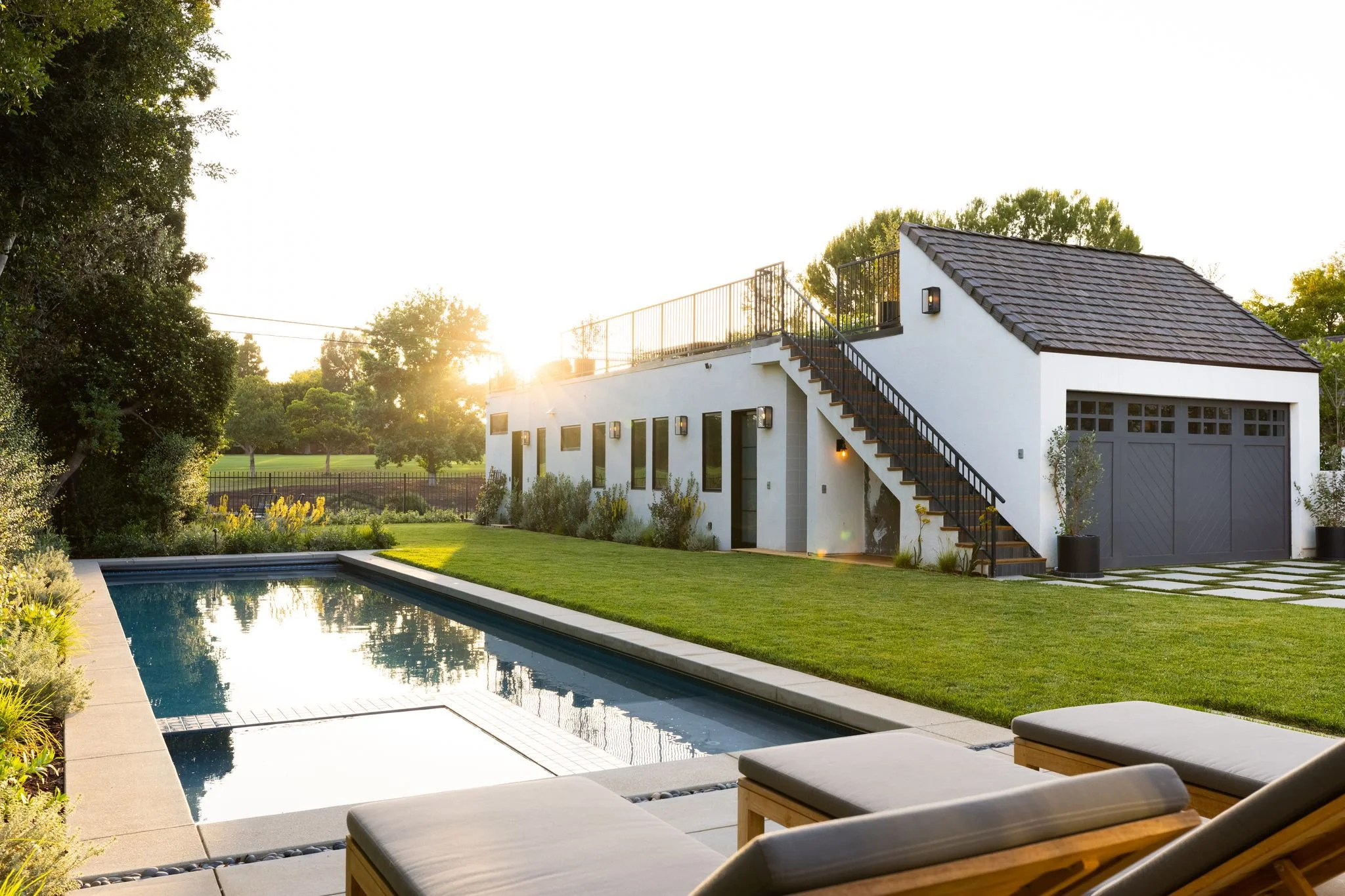 Golf course estate with clean lines against classic Tudor, layered landscaping, linear pool, driveway, lush lawn and warm landscape lighting.