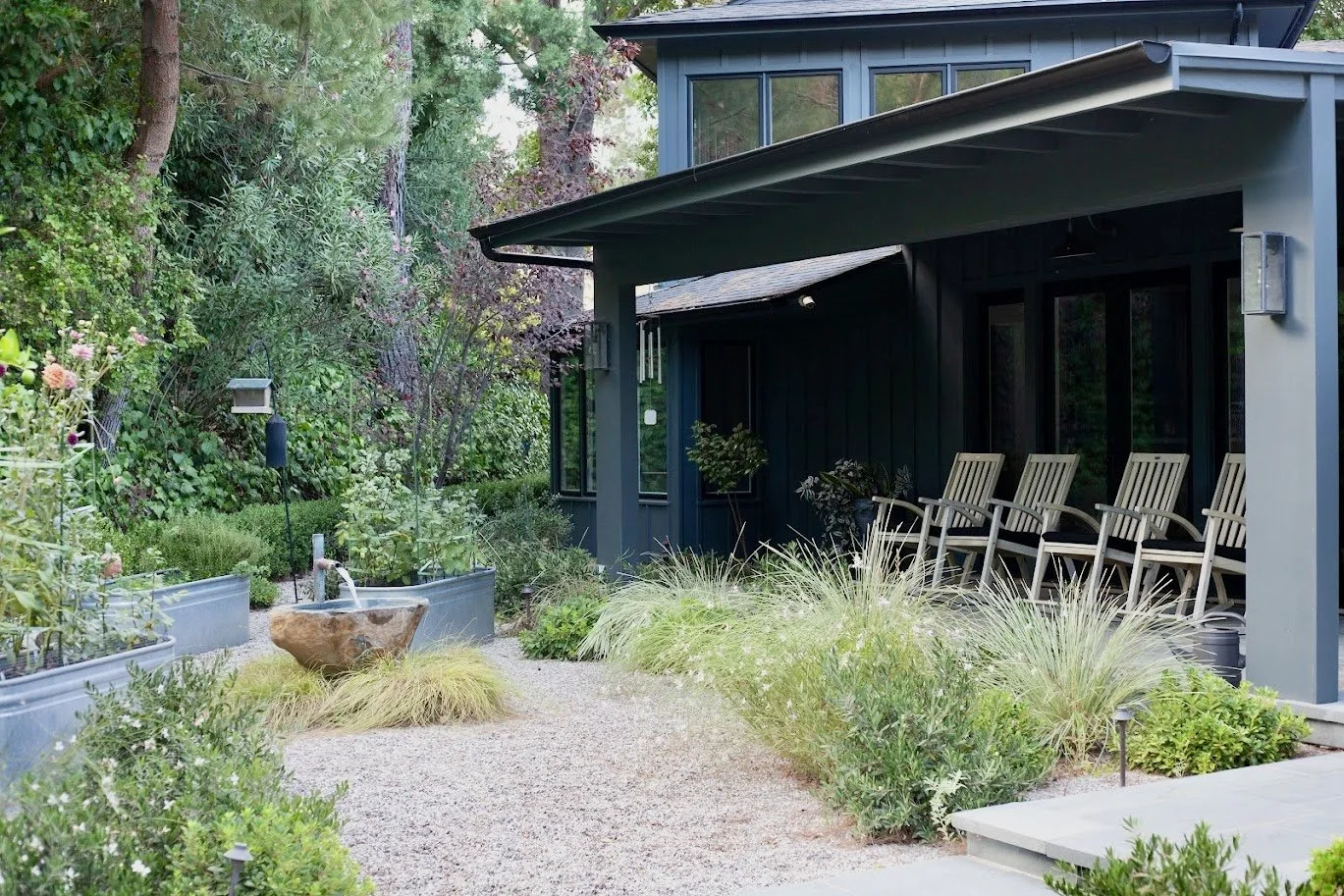 Large entertainer's yard with linear pool, chaise lounges, cantilevered umbrellas, fire pit gravel lounge, lush layered Mediterranean plantings and privacy hedges, front sitting porch, walkways through the garden.