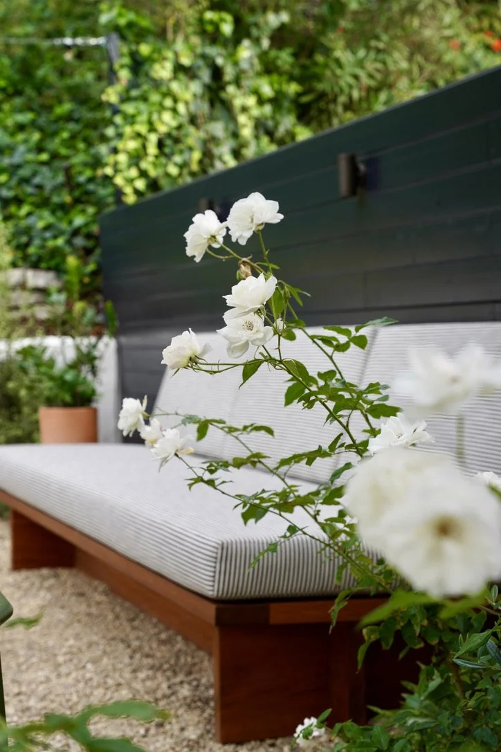 Cozy and bright yard with lush synthetic turf, fire pit lounge, play structure, horizontal slat fencing, decorative potted plantings, layered perimeter landscaping, Mexican pebbles.