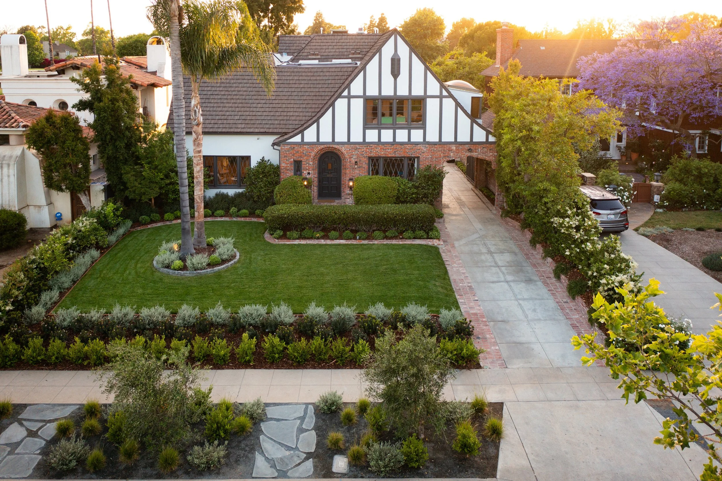 Golf course estate with clean lines against classic Tudor, layered landscaping, linear pool, driveway, lush lawn and warm landscape lighting.