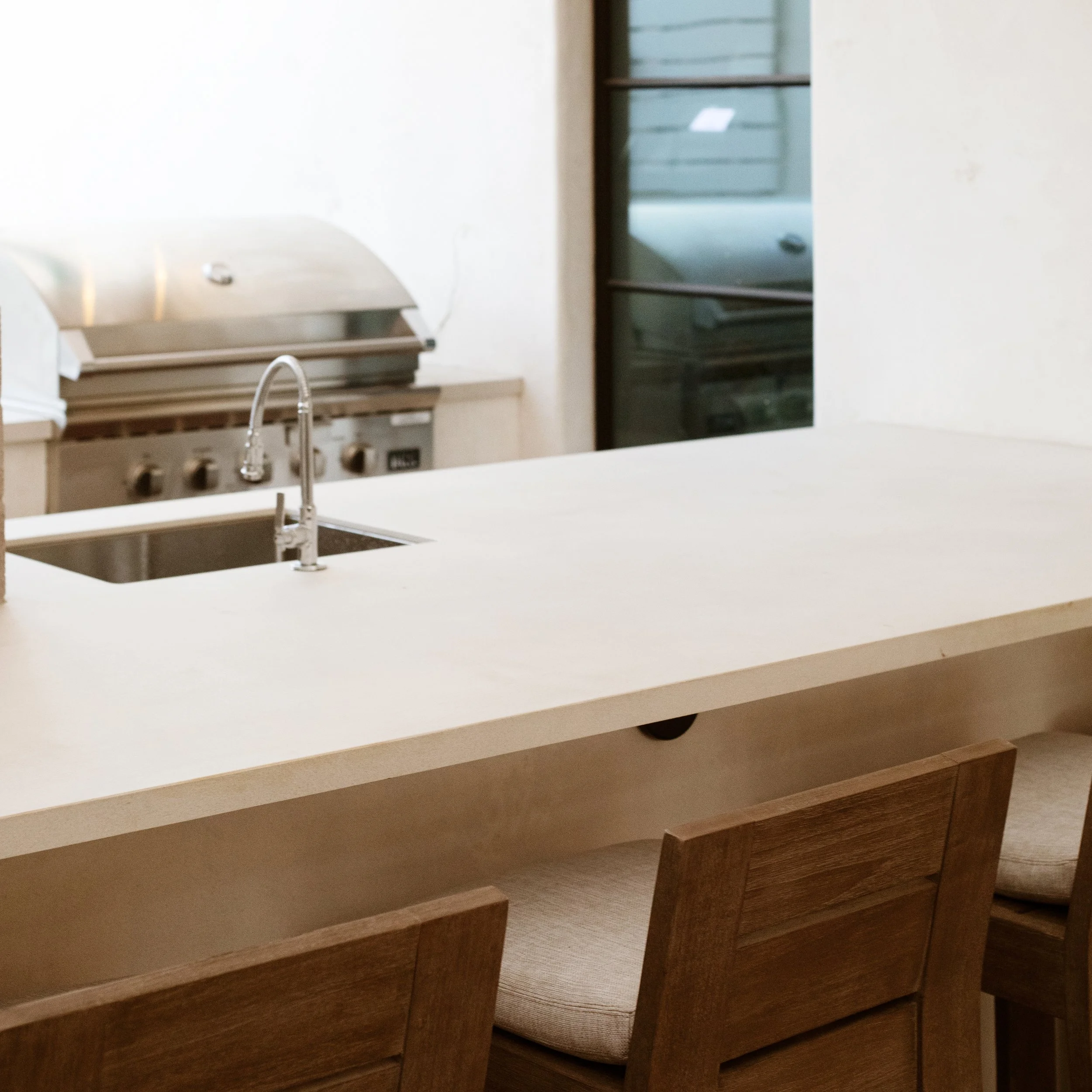 Contemporary BBQ island with neutral colors, sink, grill and bar stools.