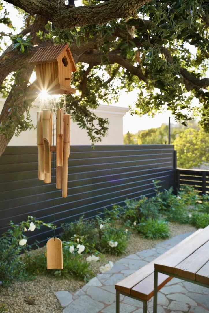 Cozy and bright yard with lush synthetic turf, fire pit lounge, play structure, horizontal slat fencing, decorative potted plantings, layered perimeter landscaping, Mexican pebbles.