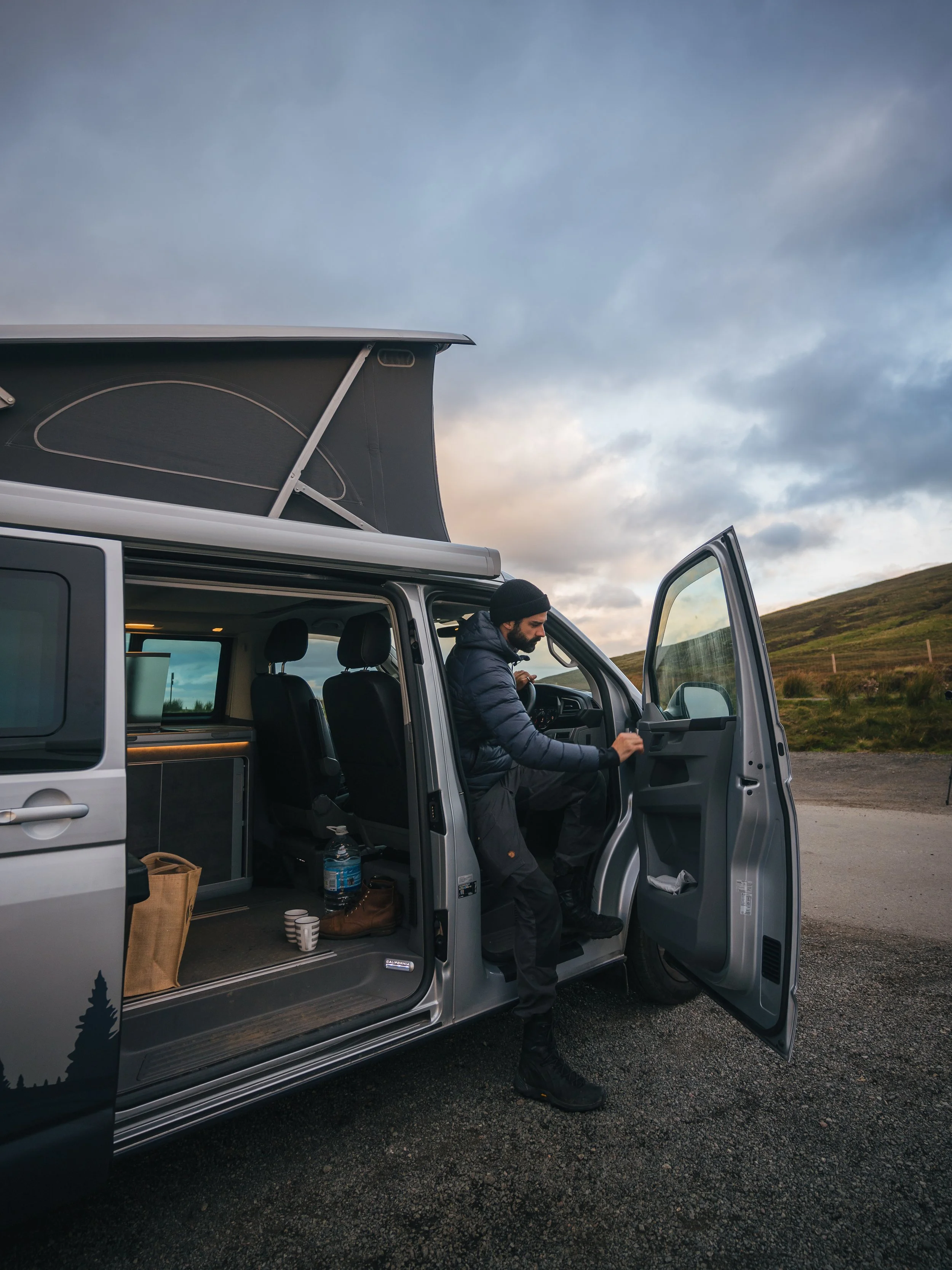 Man opening the door of a campervan in Scotland. It's from camper van rental in Glasgow, called Harris Campers. Campervan hire Scotland