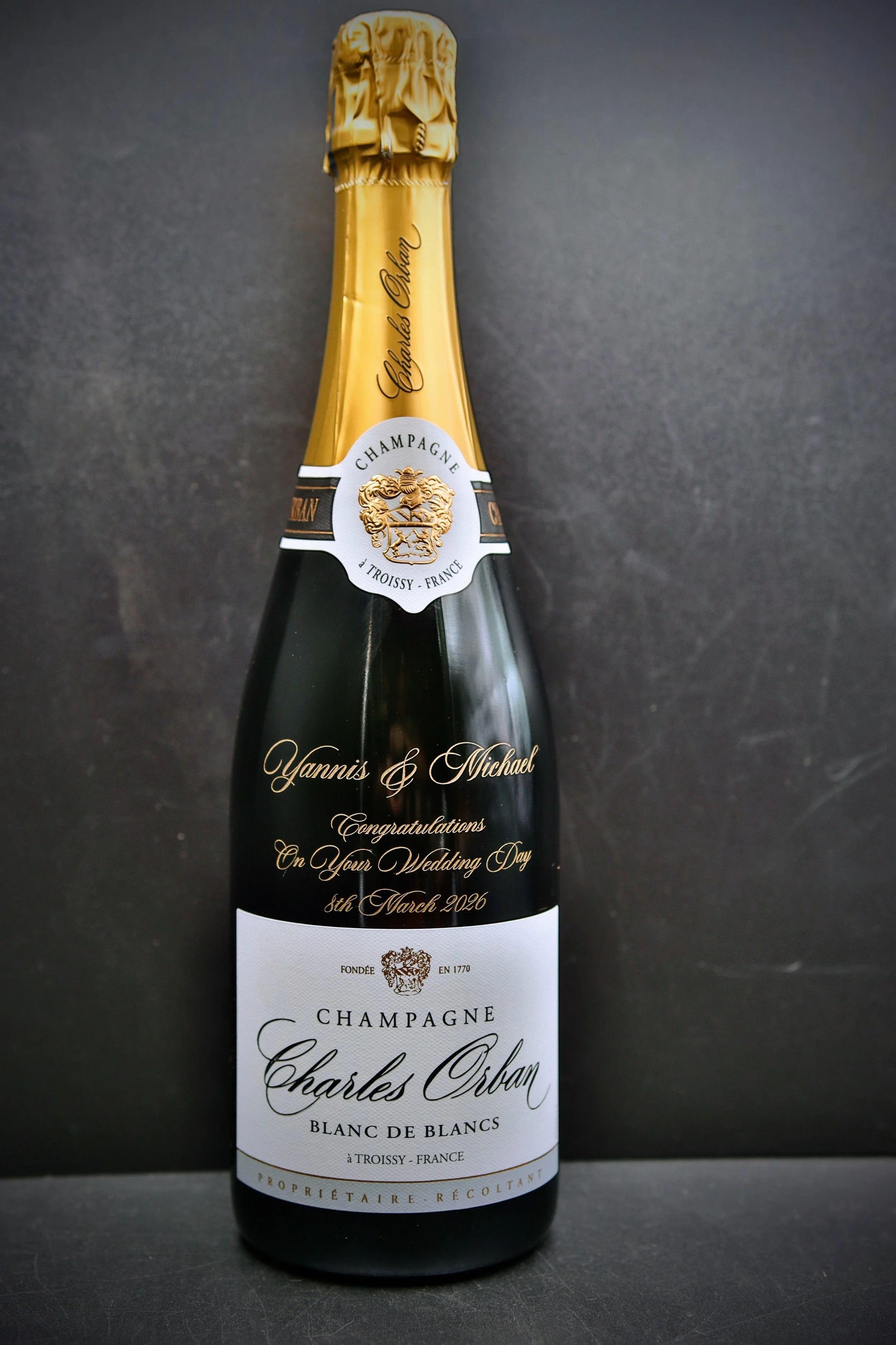 Personalized Piper-Heidsieck champagne bottle with "Happy 60th Birthday Liisa" engraving against green foliage backdrop.