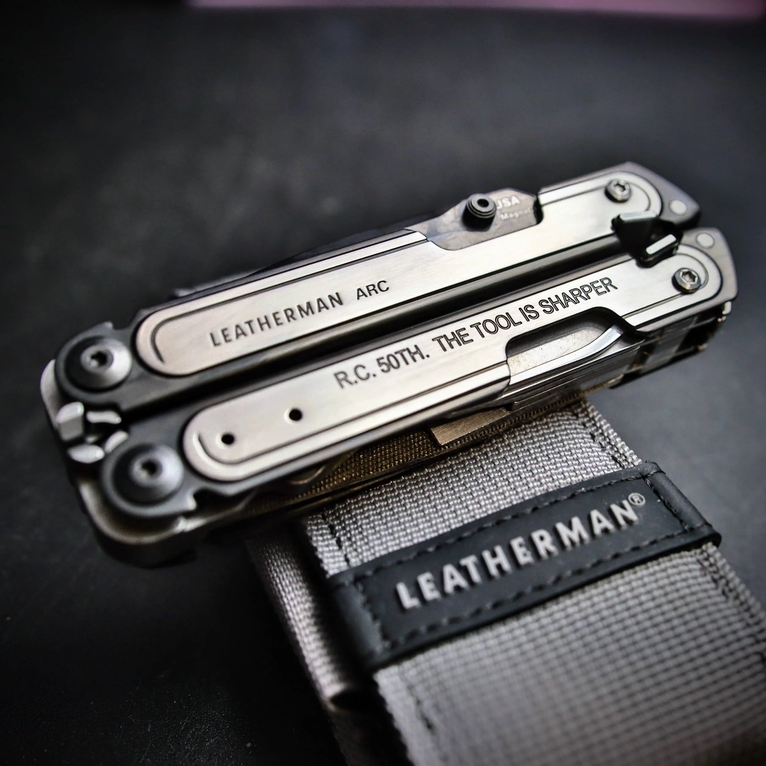 Three Leatherman Rebar multi-tool packages displayed on a wooden surface with a leafy green backdrop.